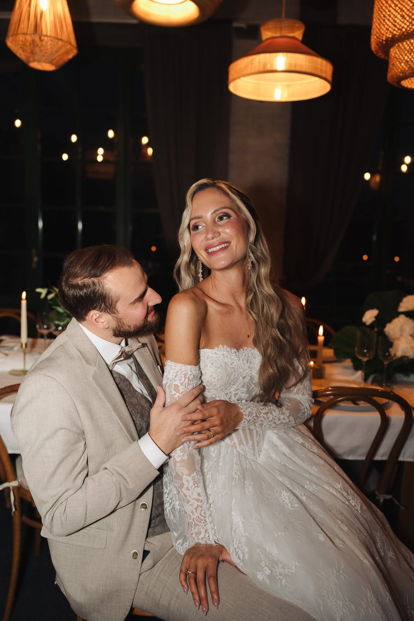 Ein Paar bei einer Hochzeit, das Brautkleid und Anzug trägt, in einem festlich gedeckten Raum mit Kerzen und warmem Licht.