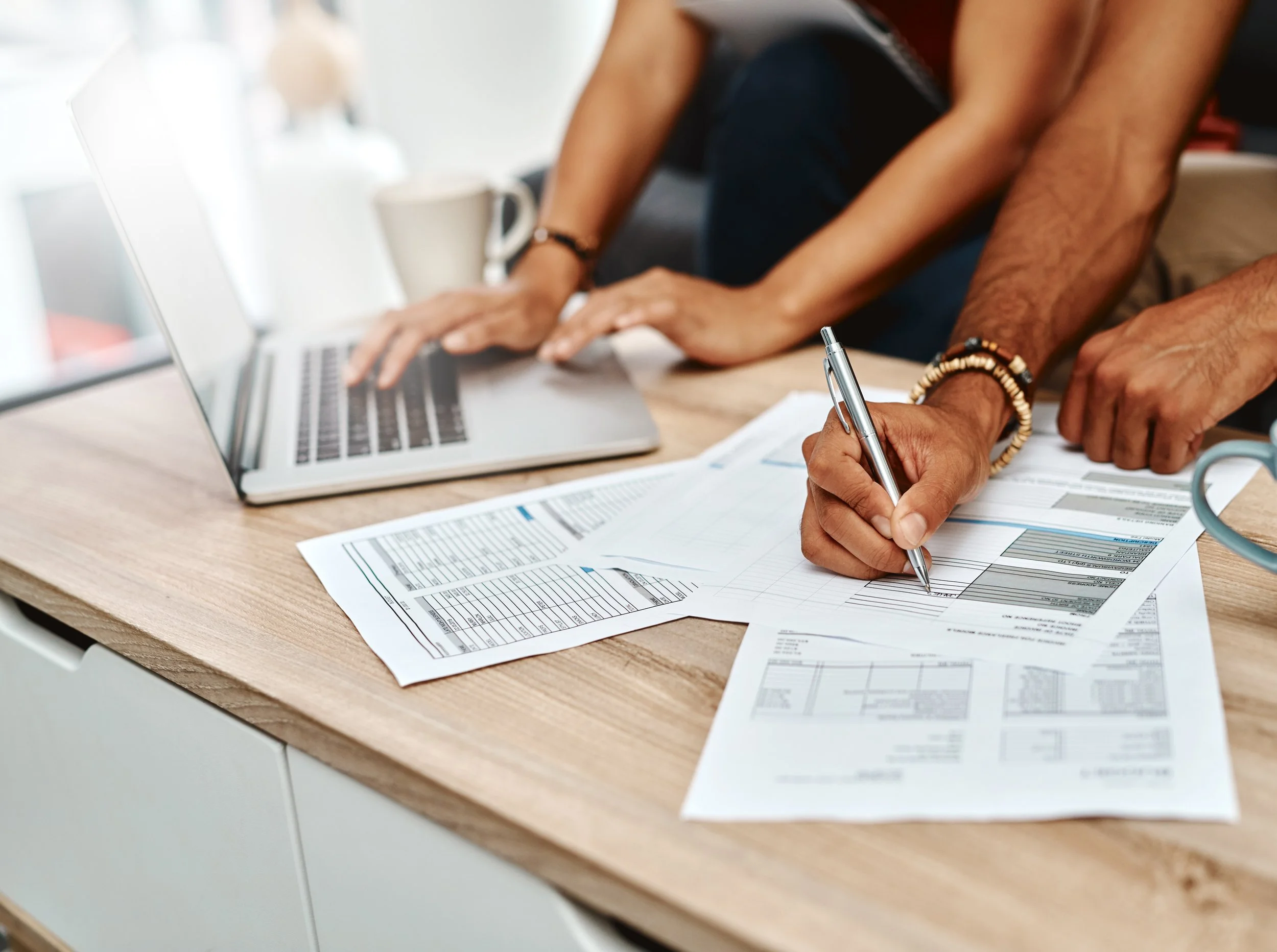 People working with financial documents and a laptop on a wooden table.