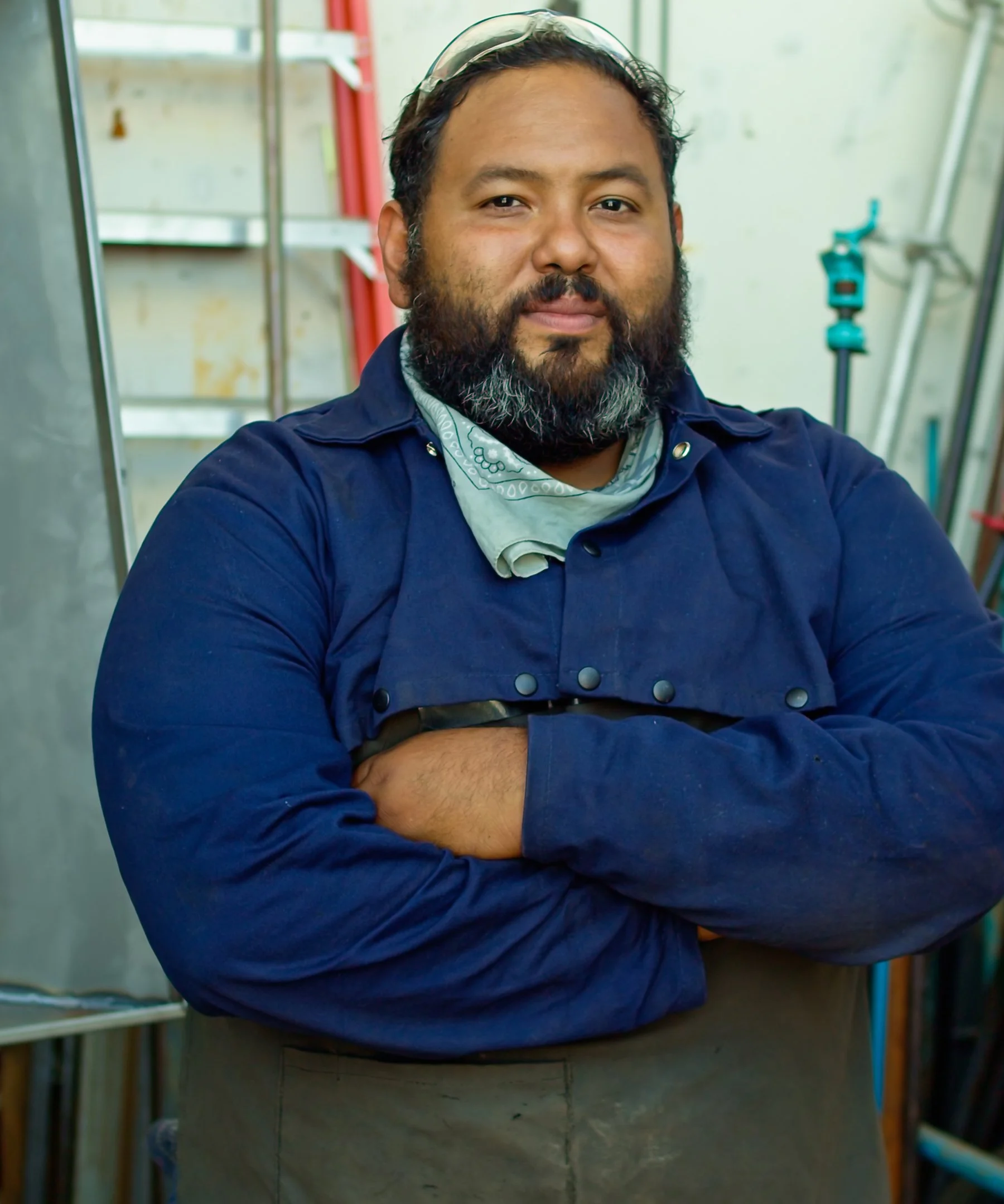 Man wearing eye protection and an apron standing at a job site. He is smiling warmly and has his arms crossed across his chest.