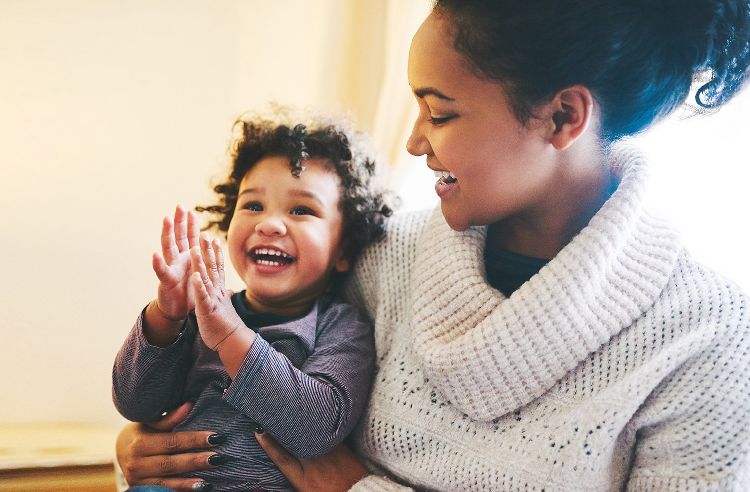 A laughing, clapping child being held by their smiling mother.