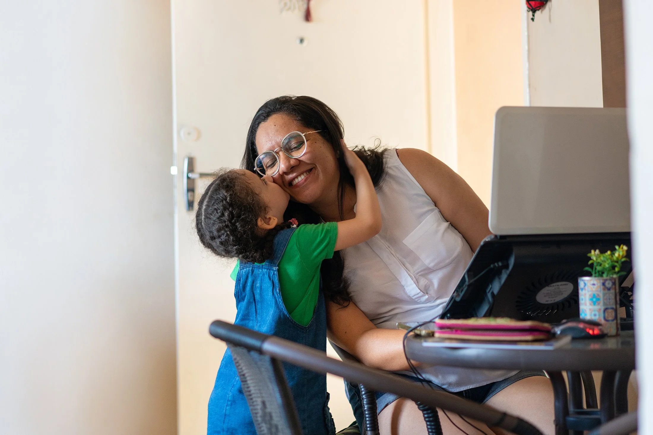 Parent working at home on a laptop computer. She is taking a break to hug her small child.