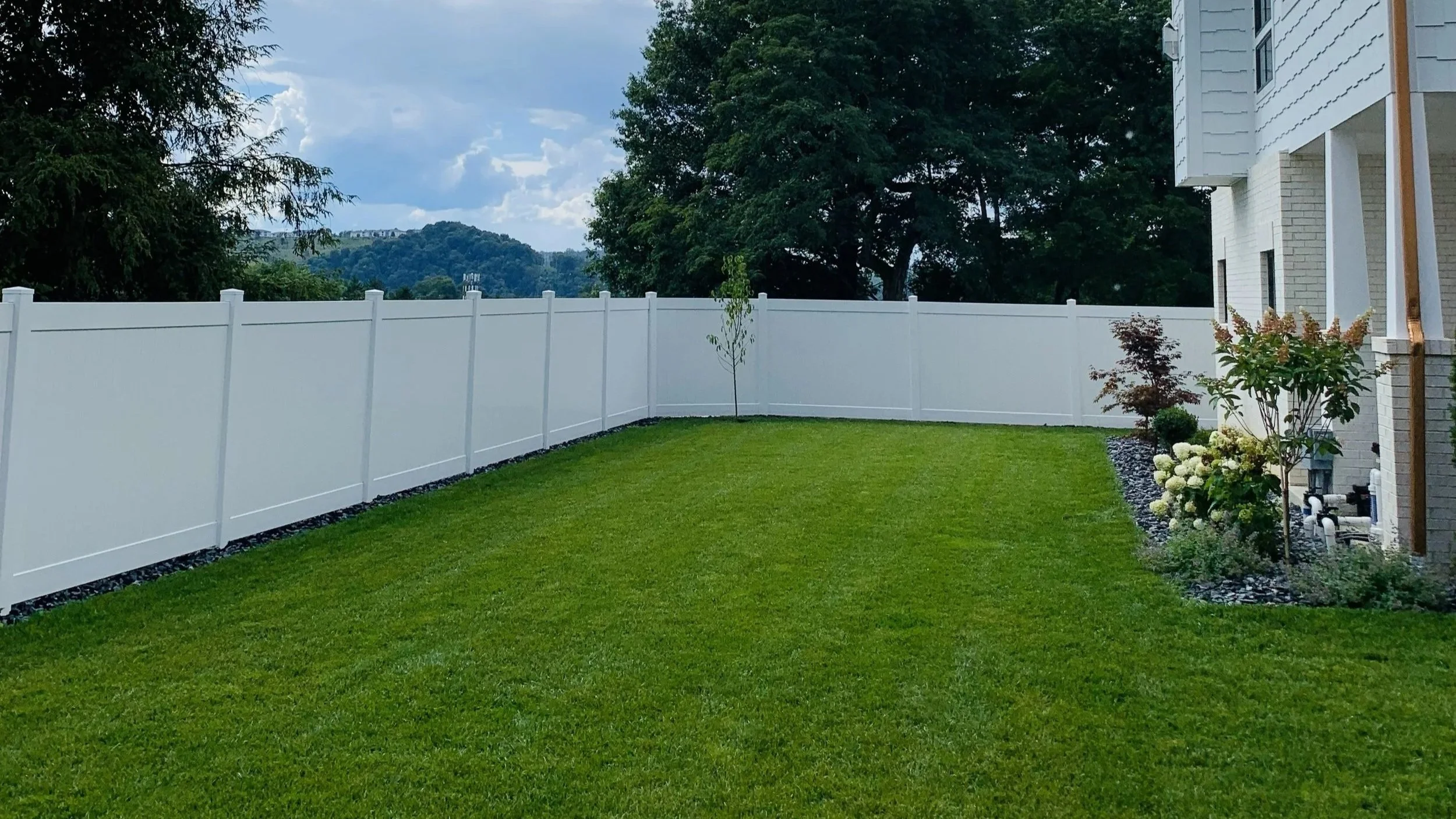 Modern house backyard with swimming pool, wooden deck, outdoor seating, potted plants, and glass sliding doors leading inside.