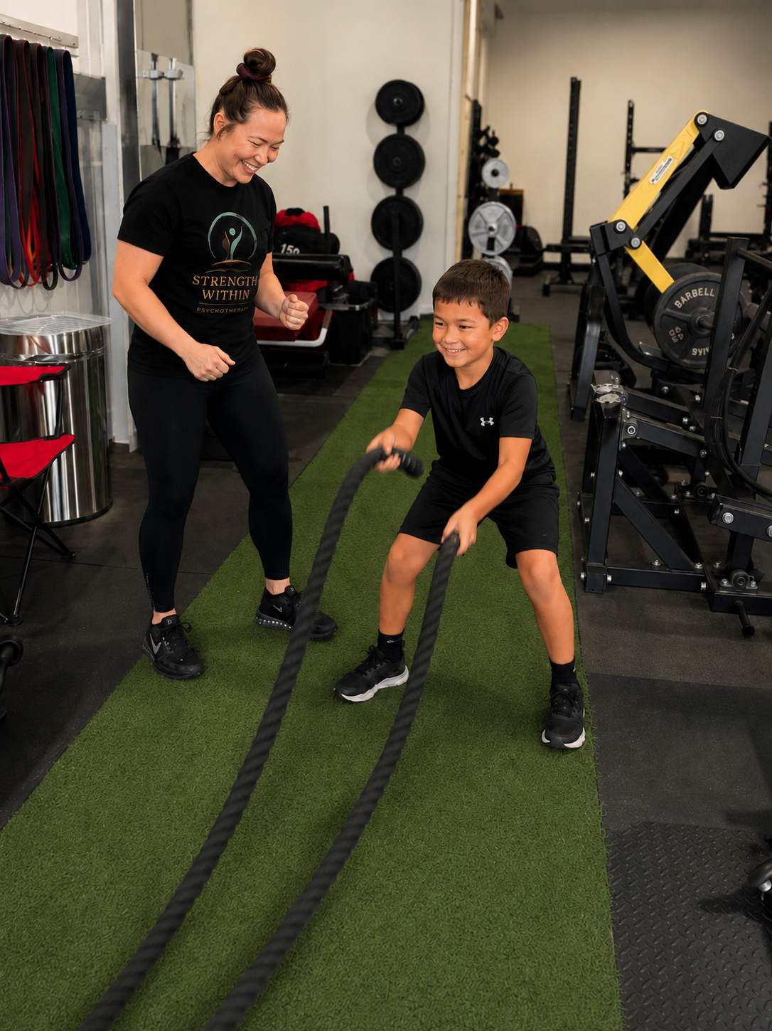 Movement and Exercise Psychotherapy therapist supporting a smiling child performing battle ropes in a private Orangeville gym.