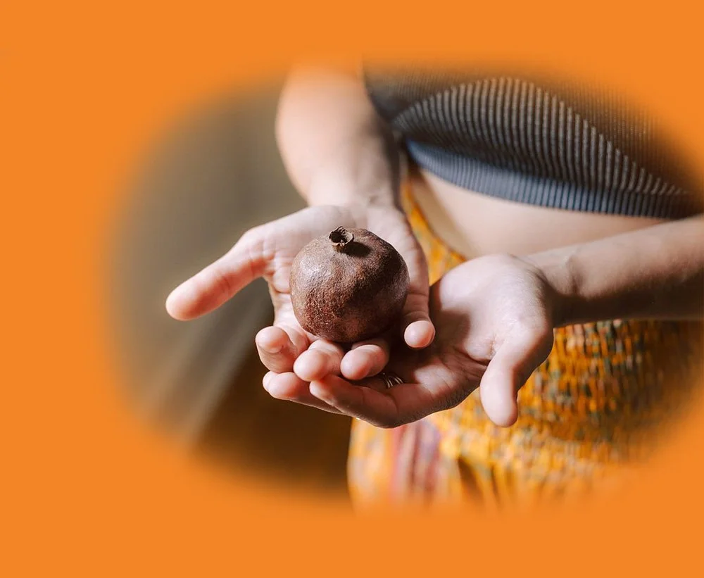 Person holding a small pomegranate fruit in their hand with a blurred orange background.