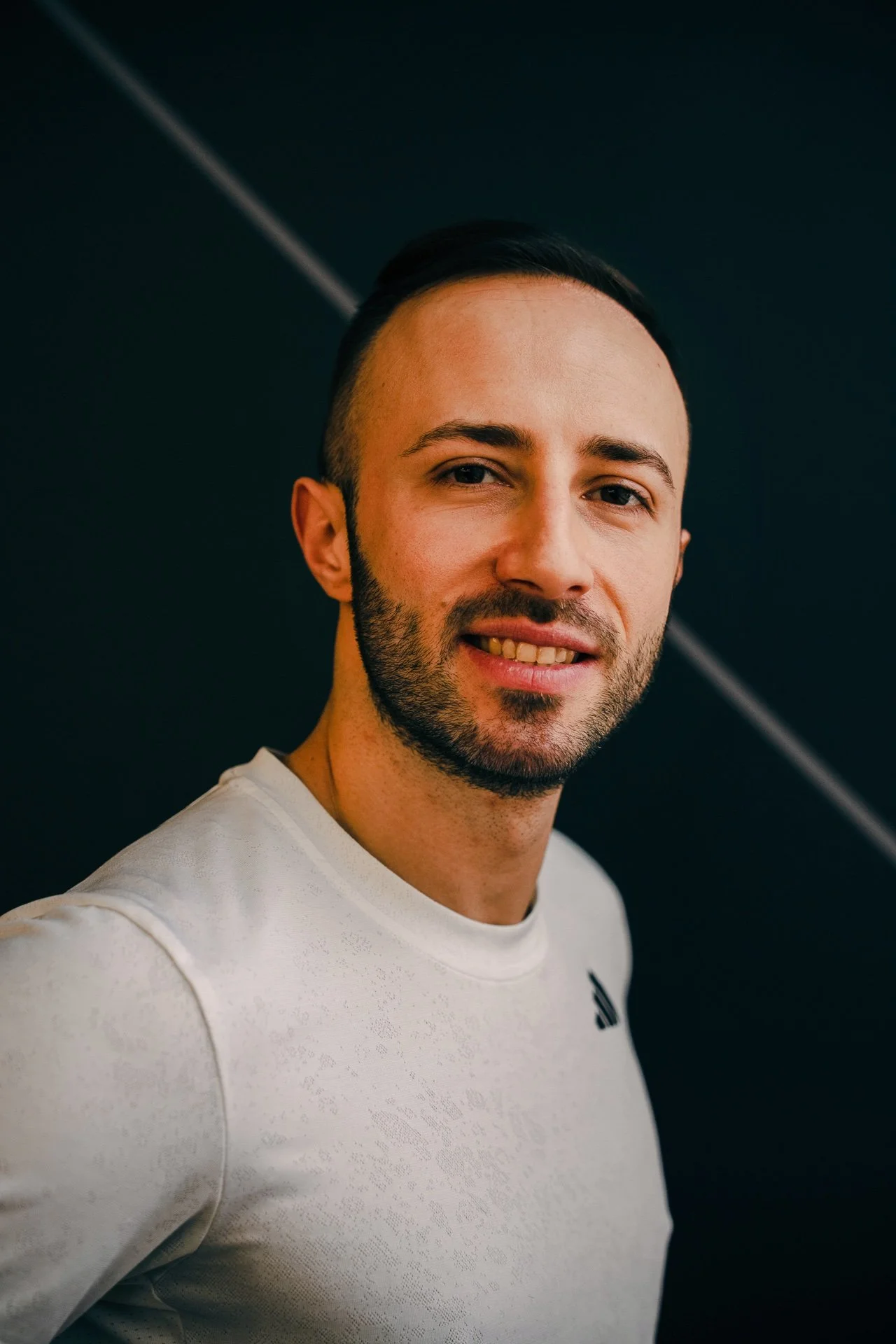 Ragazzo con barba e capelli corti, indossa una maglietta bianca, sfondo nero