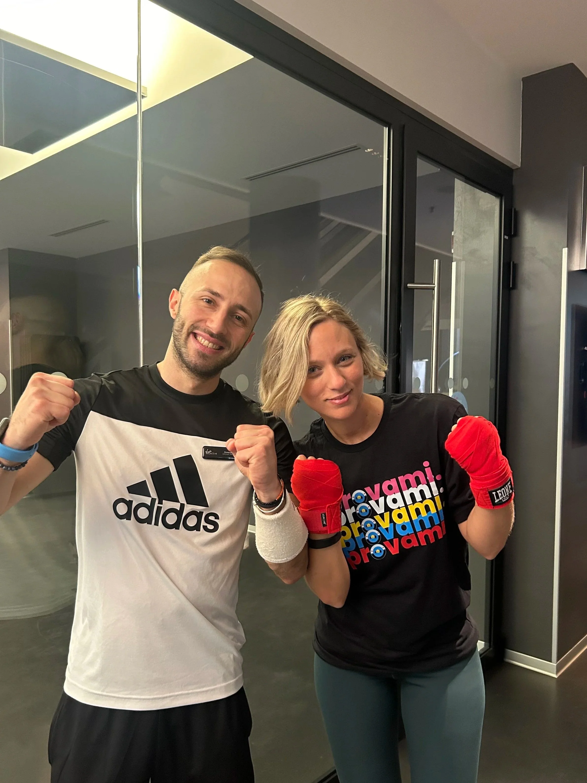 Due persone in abbigliamento sportivo, una con guantoni rossi, in posa da combattimento in una palestra di boxe o arti marziali.