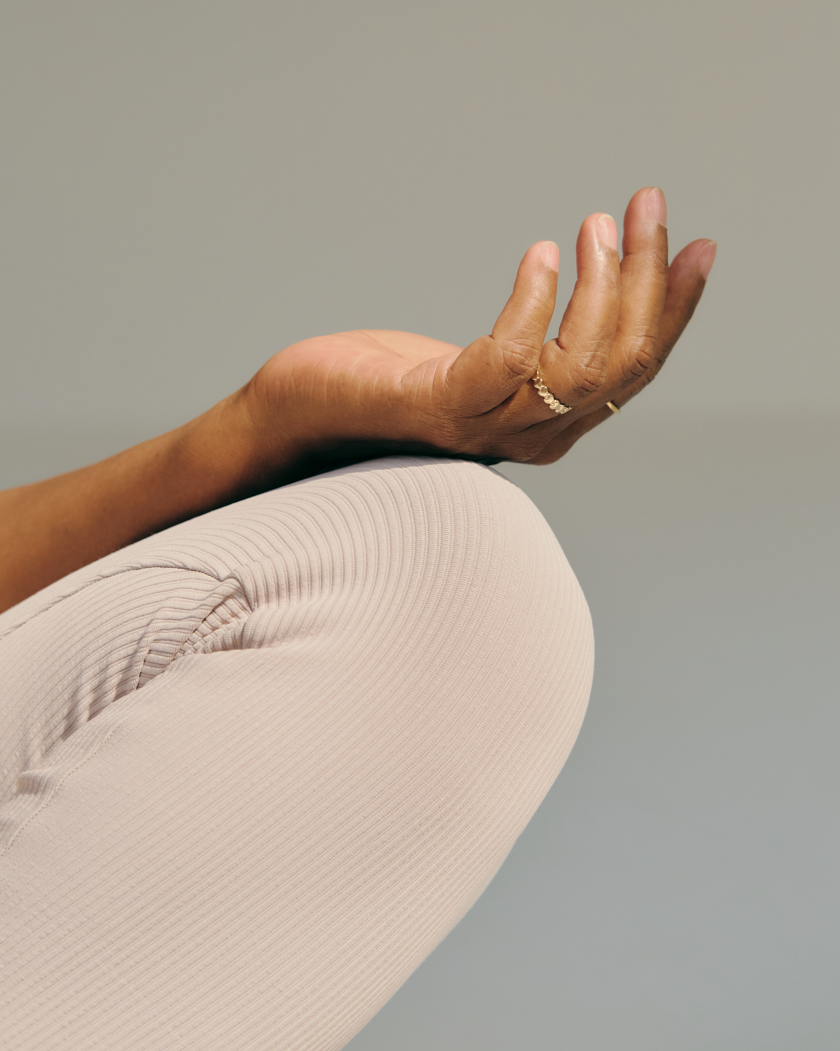 Close-up of a person's arm resting on their bent knee, with the hand raised and fingers slightly spread, wearing rings.