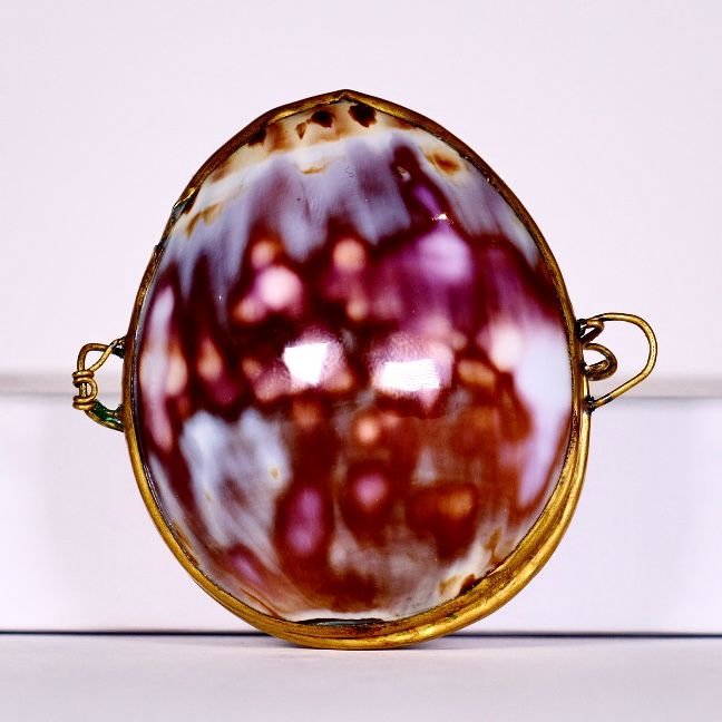 Close-up of a decorative glass or ceramic piece resembling a rusty, abstract face with a purple and white color pattern, mounted on a white surface.