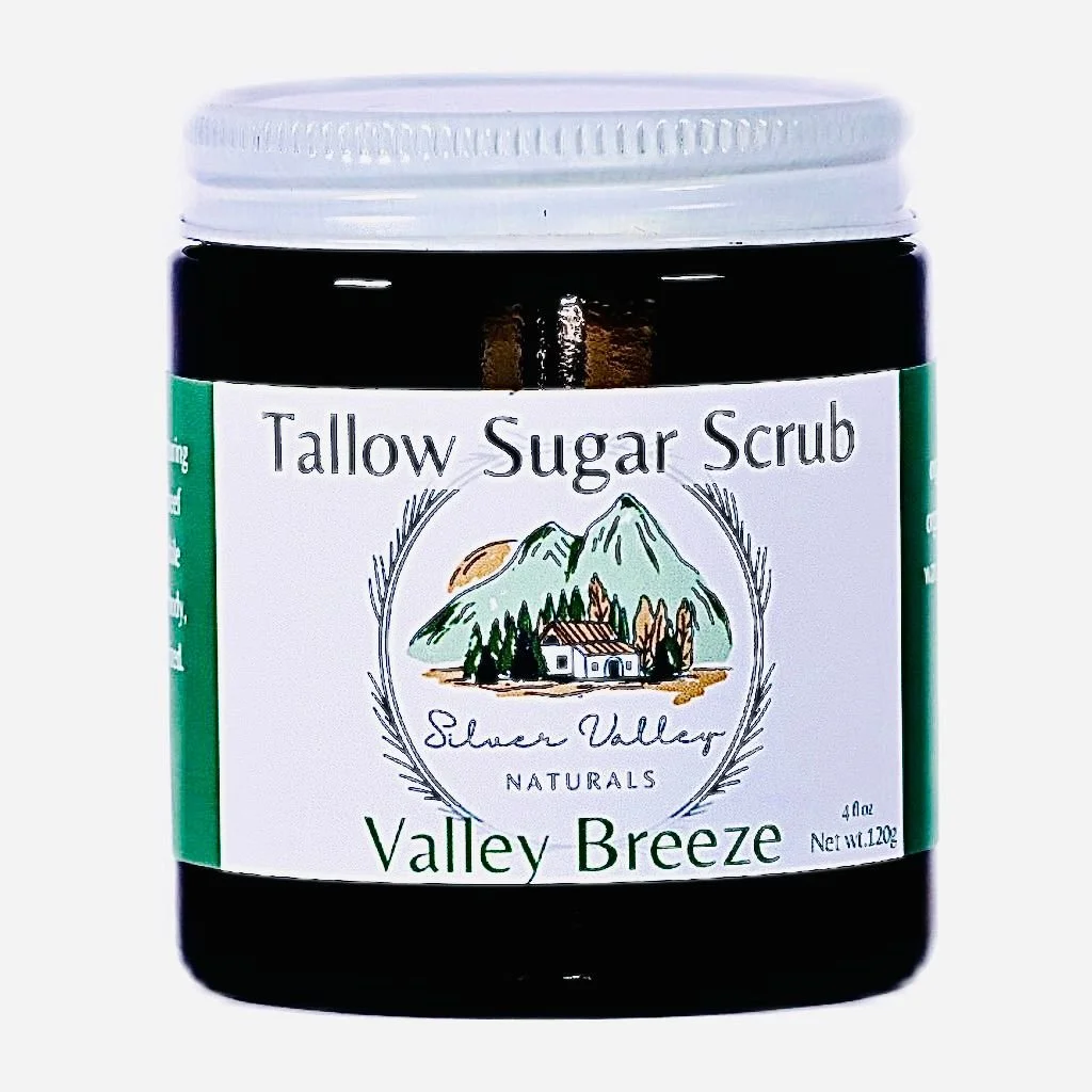 A black jar of Tallow Sugar Scrub labeled Valley Breeze. The label features an illustration of mountains, trees, and a house, and states it is a natural product from Silver Valley Naturals.