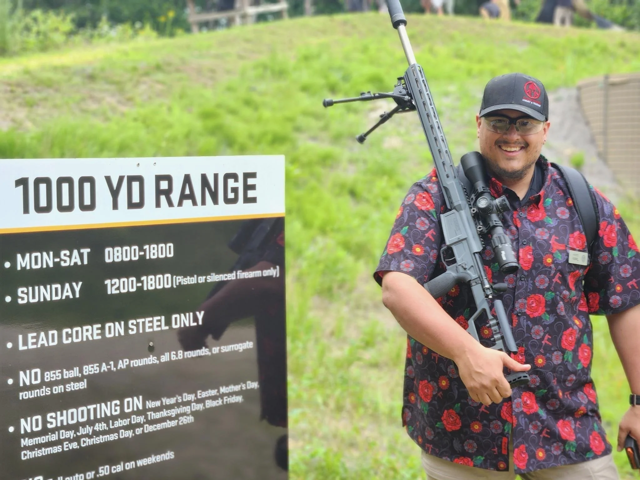 Teddy Collins, Candidate for Colorado State Senate District 4 in sunglasses and a black cap holding a rifle on his shoulder at a shooting range with a sign displaying rules and guidelines.