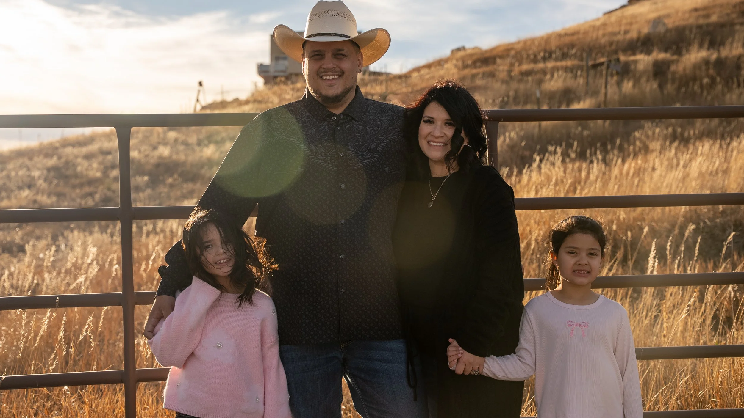  Teddy Collins, Candidate for Colorado SD 4 together with his family outdoors by a fence in a hilly, grassy area during sunset.
