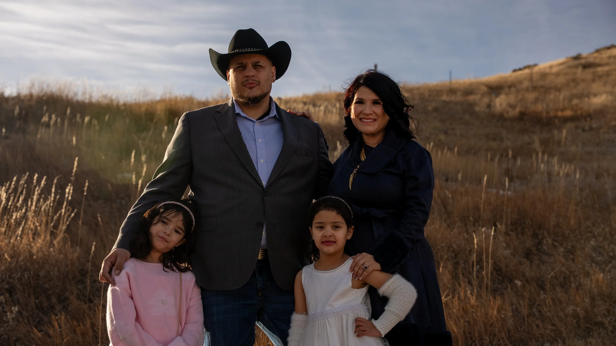 Teddy Collins, Candidate for Colorado State Senate District 4 posing outside with his family for a photo with a grassy, hill landscape in the background during sunset.
