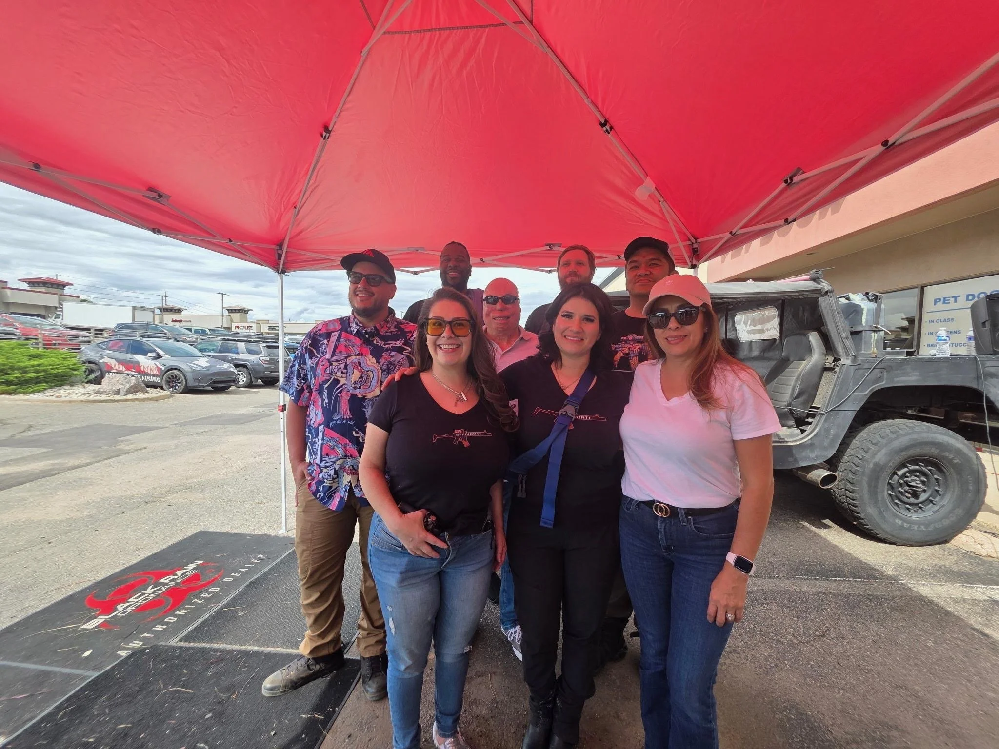 Teddy Collins, Candidate for Colorado State Senate District 4 and a group of constituents smiling under a red canopy, standing in front of a black vehicle in a parking lot.