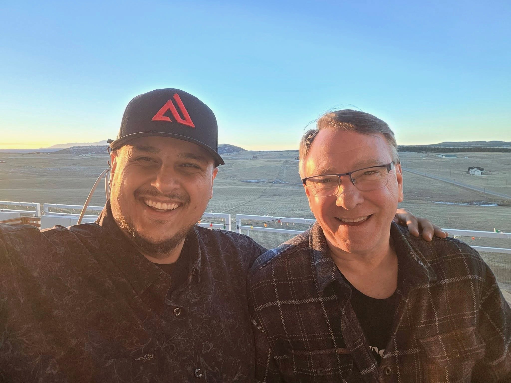 Teddy Collins, Candidate for Colorado SD 4 with a man smiling and taking a selfie outdoors during sunset, with open field and a few small houses in the background.
