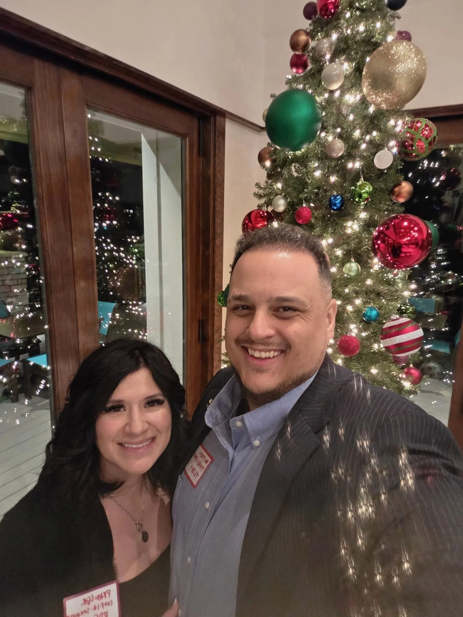 Teddy Collins, Candidate for Colorado SD 4 and his wife taking a selfie in front of a decorated Christmas tree with colorful ornaments and lights.