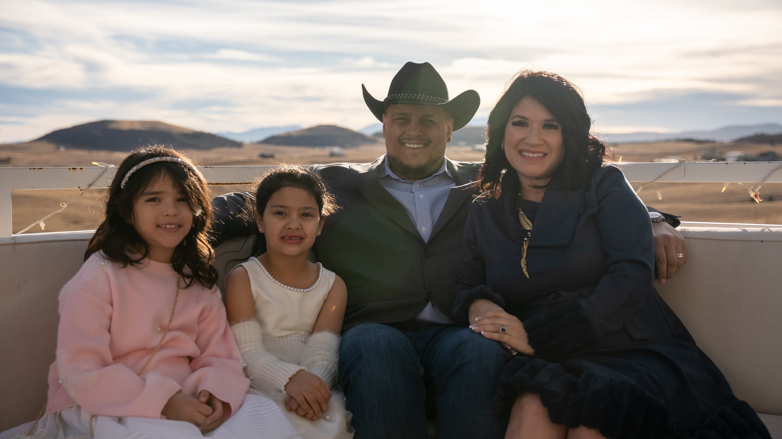 Teddy Collins, Candidate for Colorado State Senate District 4 and his family sitting with a scenic landscape of hills and mountains in the background, during daytime.