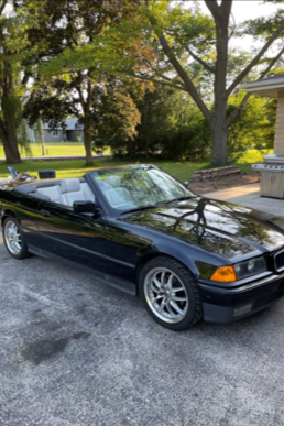 Black convertible car parked on a driveway with trees and greenery in the background