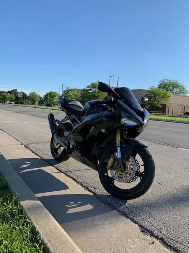 Black sport motorcycle parked on the curbside of a street on a sunny day.