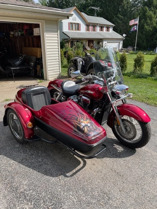 A red motorcycle with a sidecar parked in a driveway in front of a house.