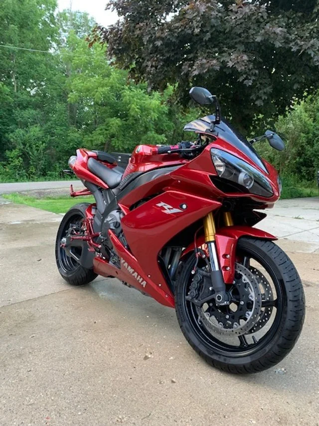 Red Yamaha YZF motorcycle parked on a concrete driveway with green trees and purple-leafed tree in background.