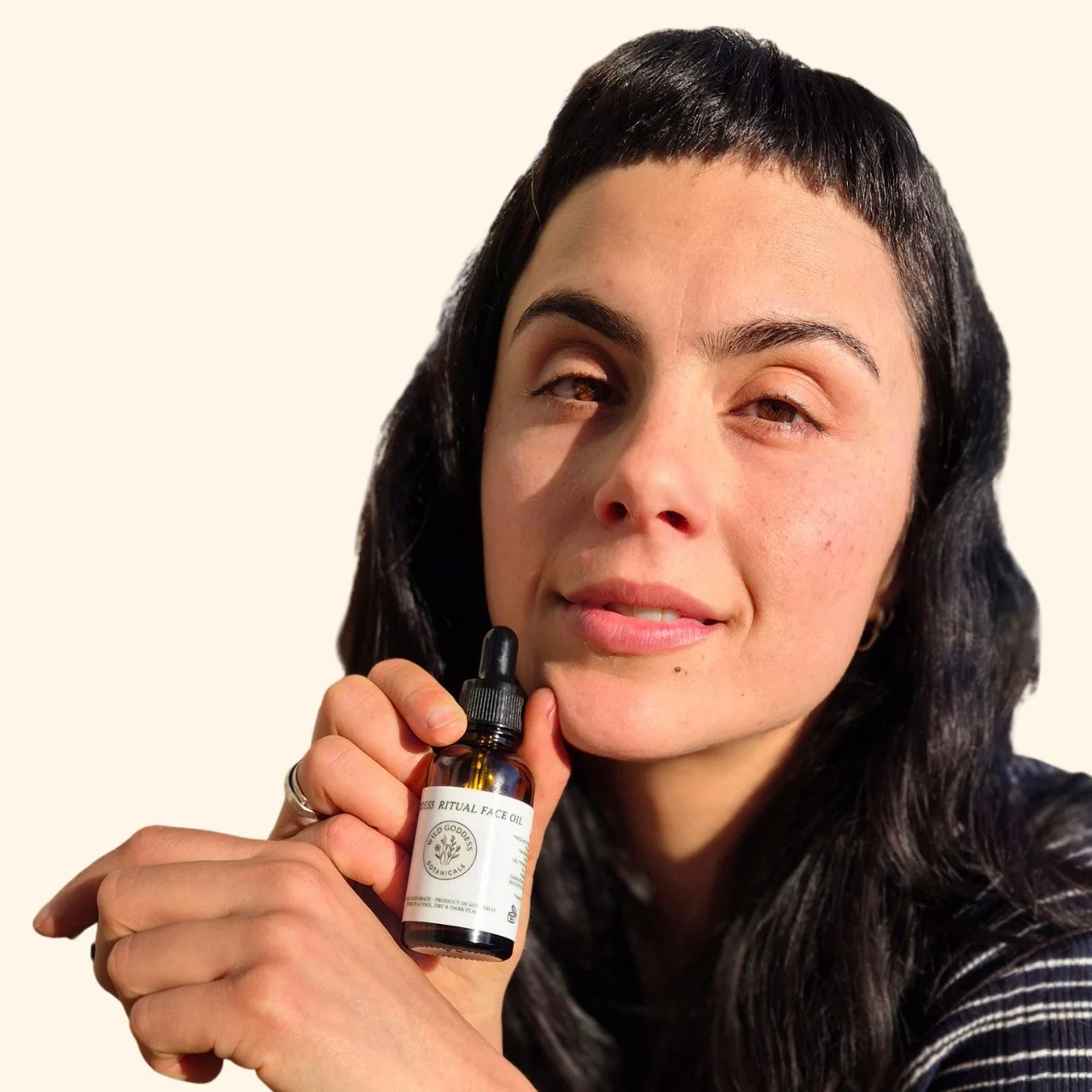 A customer holding the Goddess Ritual Face Oil bottle beside her face