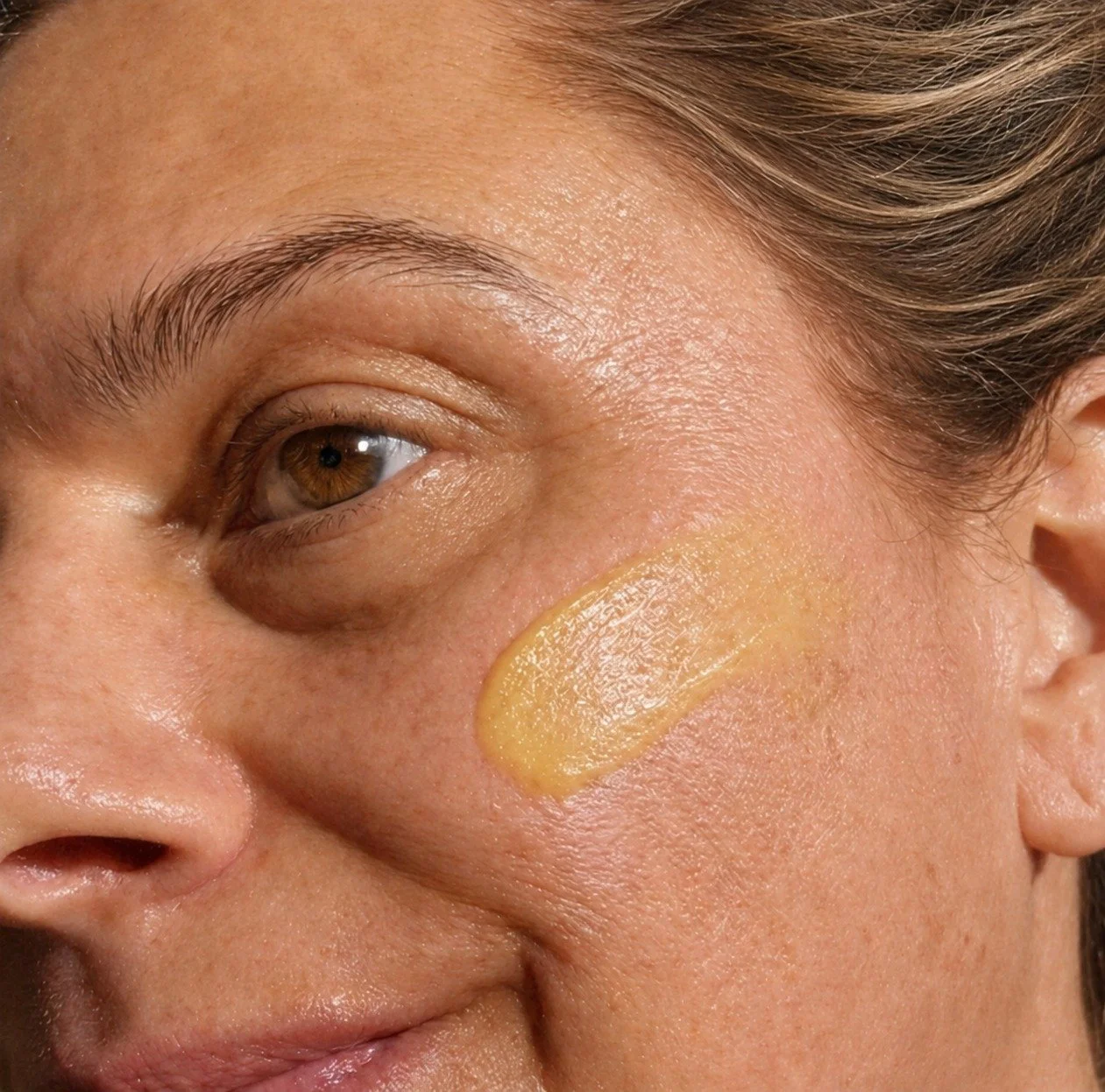 Close-up of a cheek with a swatch of Goddess Glow Face Balm on the skin