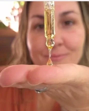 A drop of golden face oil falling from a glass dropper into an open palm