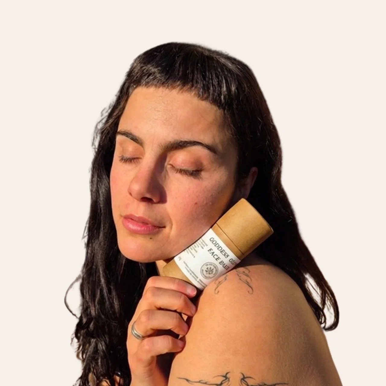 A woman holding the Goddess Glow Face Balm tube to her shoulder, eyes closed