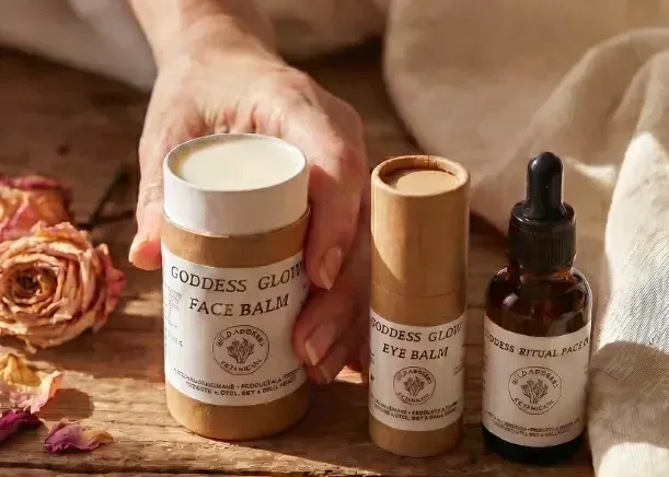 Wild Goddess Botanicals balms and face oil arranged with dried flowers on a timber surface