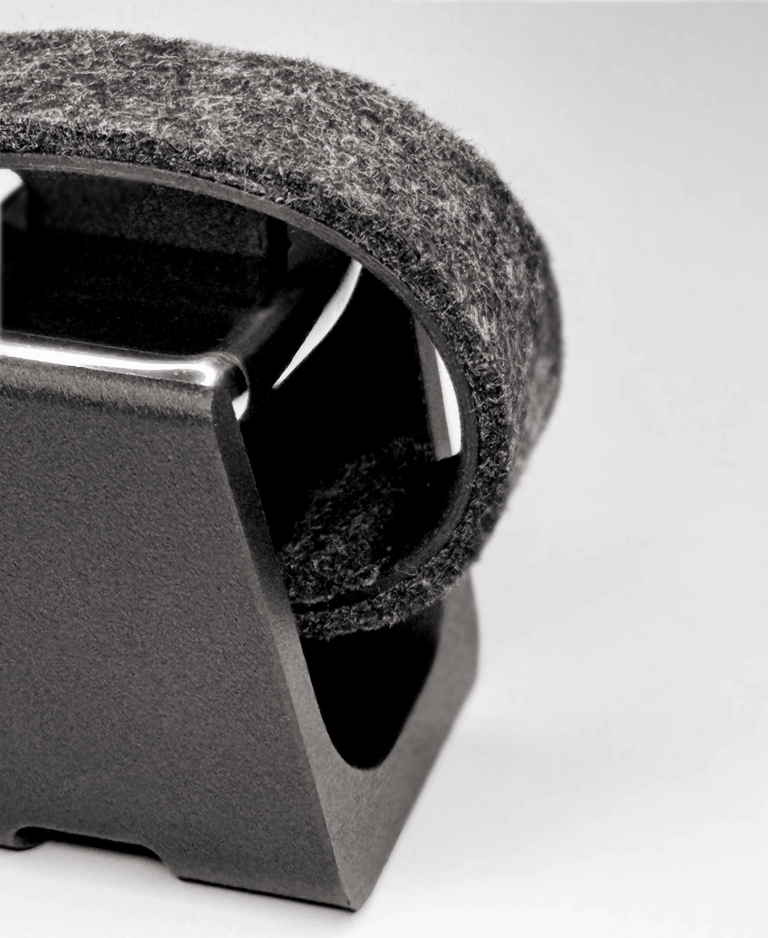 Close-up of the top of the watch.sys holder showing textured edges of the base and a gray felt surface of the carrier and the stainless steel keystone