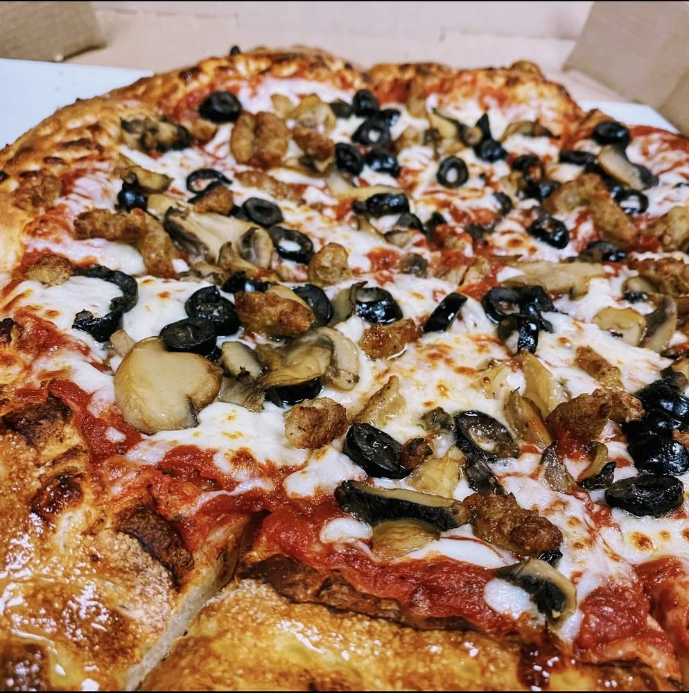 A close-up photo of a pizza with mushrooms, black olives, and pieces of cooked chicken or sausage.