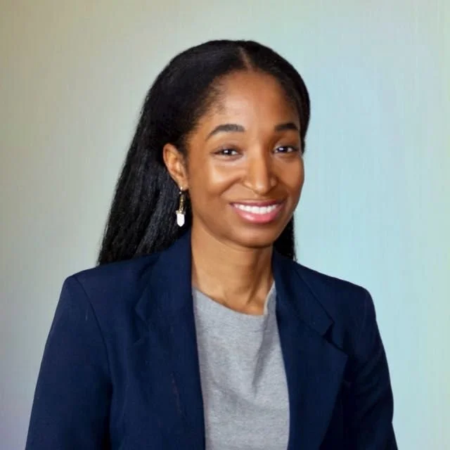 A professional woman with long black hair wearing a dark blue blazer and a gray top, smiling at the camera