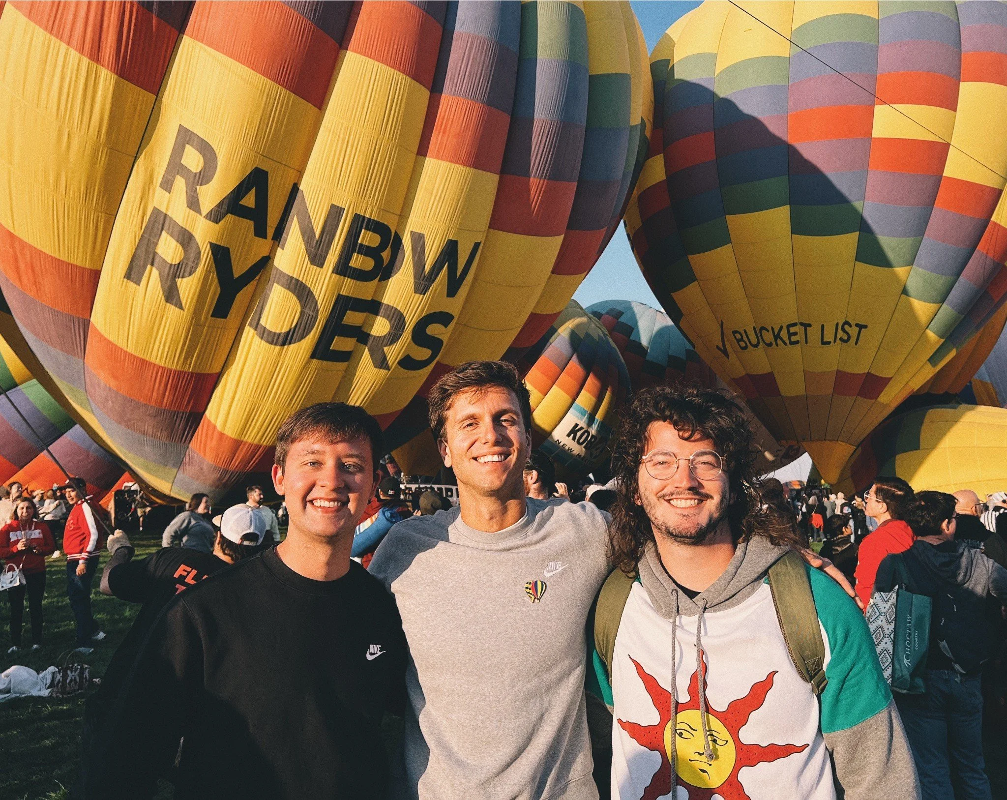 Three friends take a photo immersed by hot air balloons at the 2024 Albuquerque Balloon Fiesta.