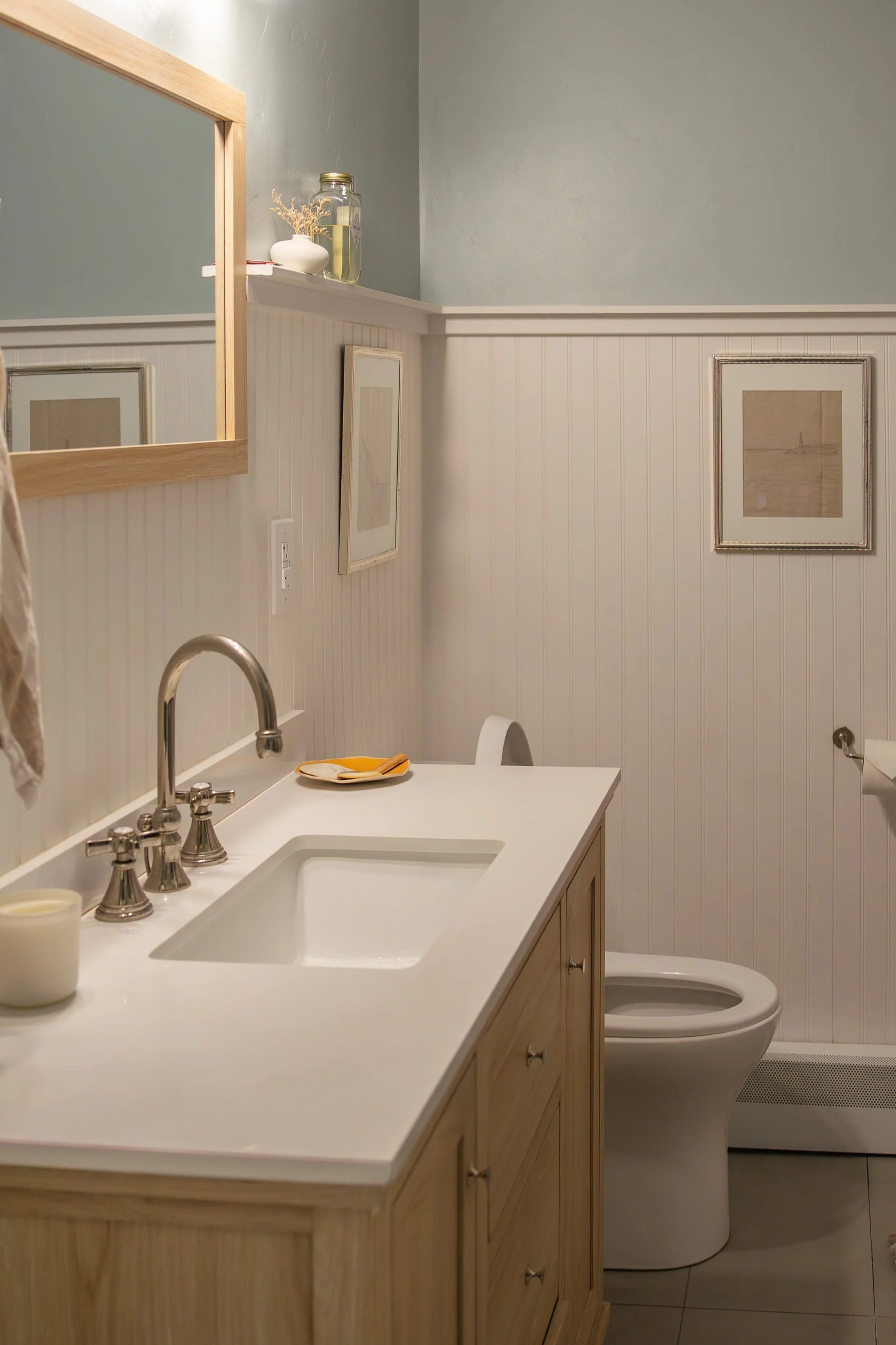 A bathroom with a white vanity, a sink, a mirror, framed wall art, a toilet, and wall-mounted light fixtures. Bozeman interior design, interior renovation, and interior styling. 