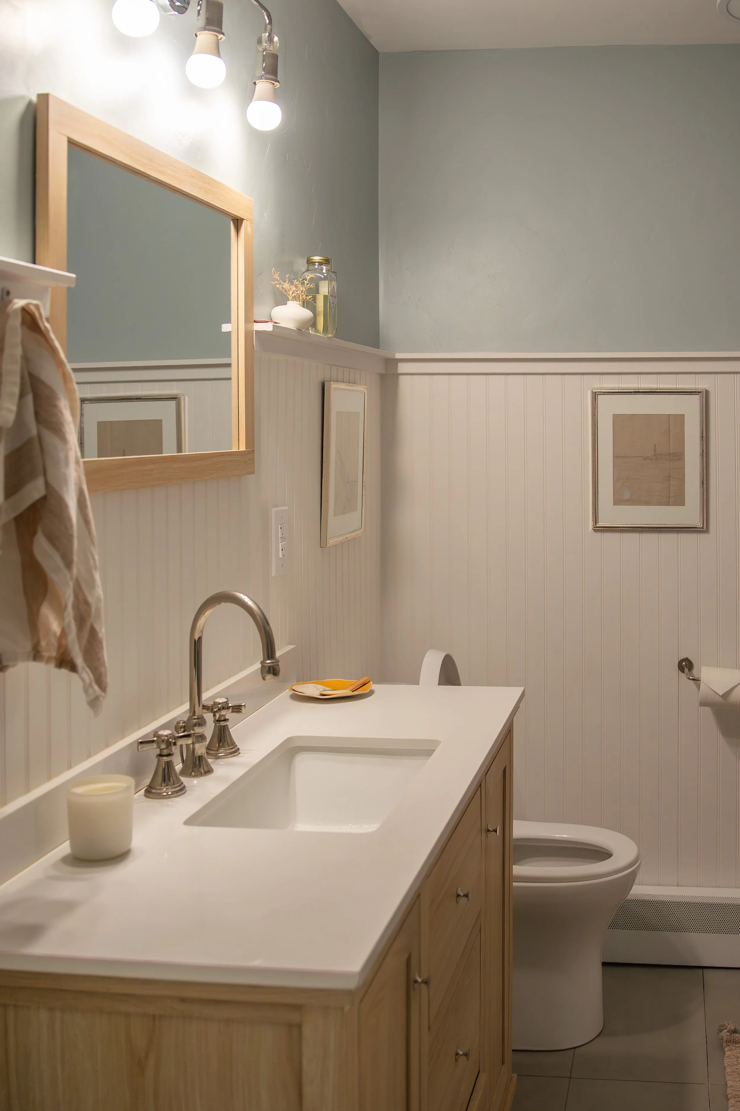 A bathroom with a white vanity, a sink, a mirror, framed wall art, a toilet, and wall-mounted light fixtures. Bozeman interior design, interior renovation, and interior styling. 