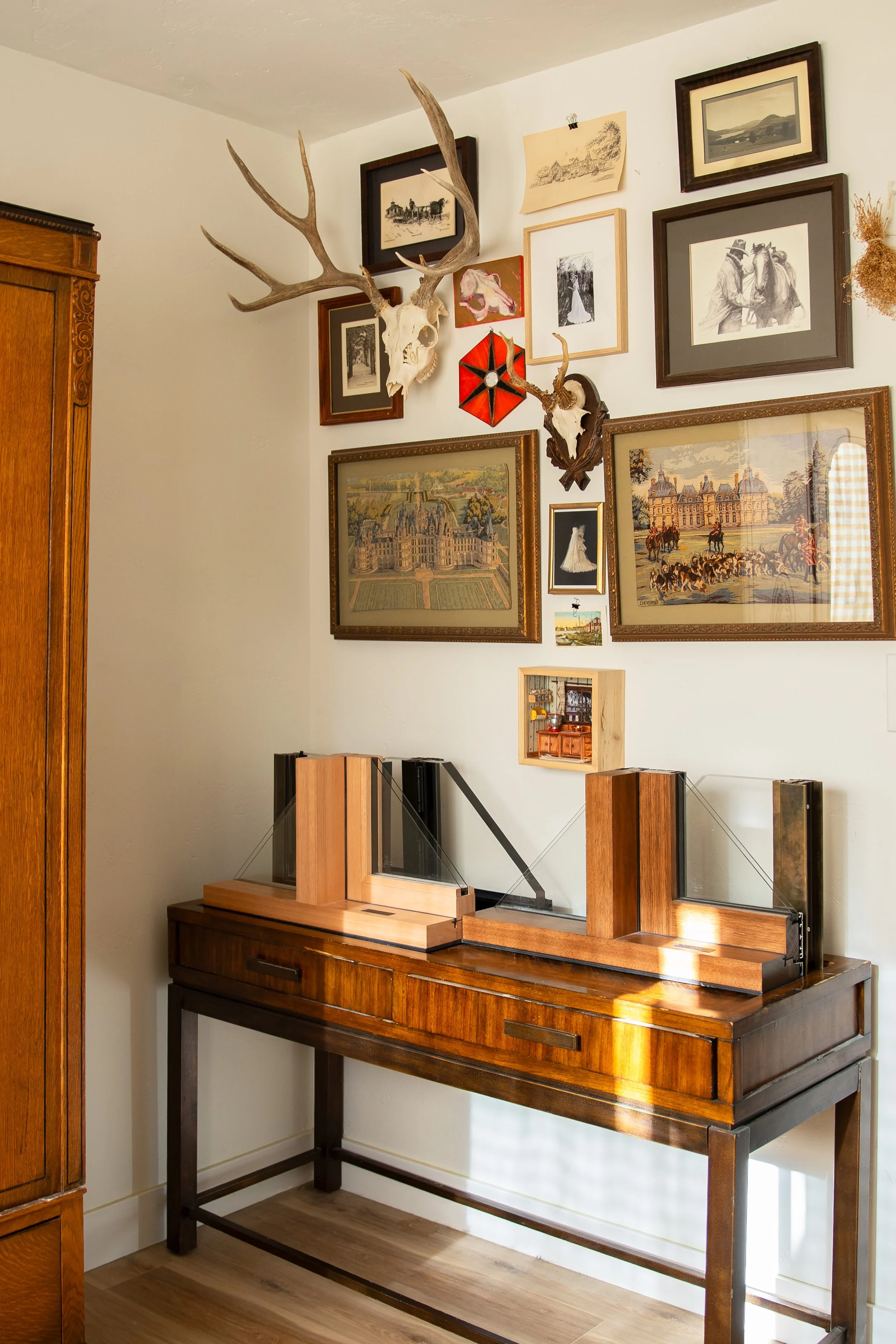 A wall decorated with framed artwork, pictures, and mounted antlers. There is a wooden console table beneath with window samples on top. Bozeman interior design, interior renovation, and interior styling. 