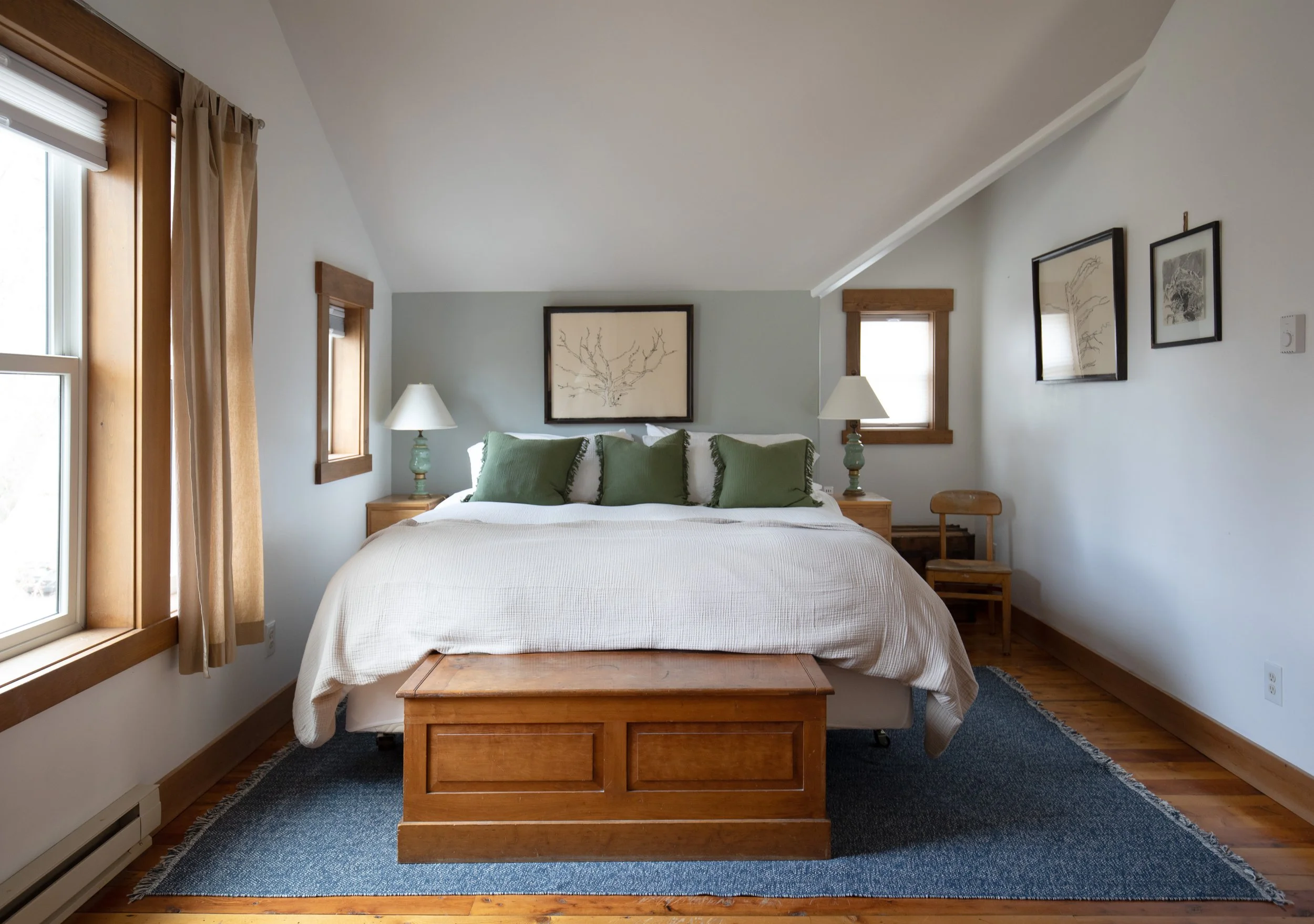 A cozy bedroom with a large bed, green pillows, wooden furniture, and framed artwork on the walls. refresh renovation remodel interior designer bozeman montana two dot interiors