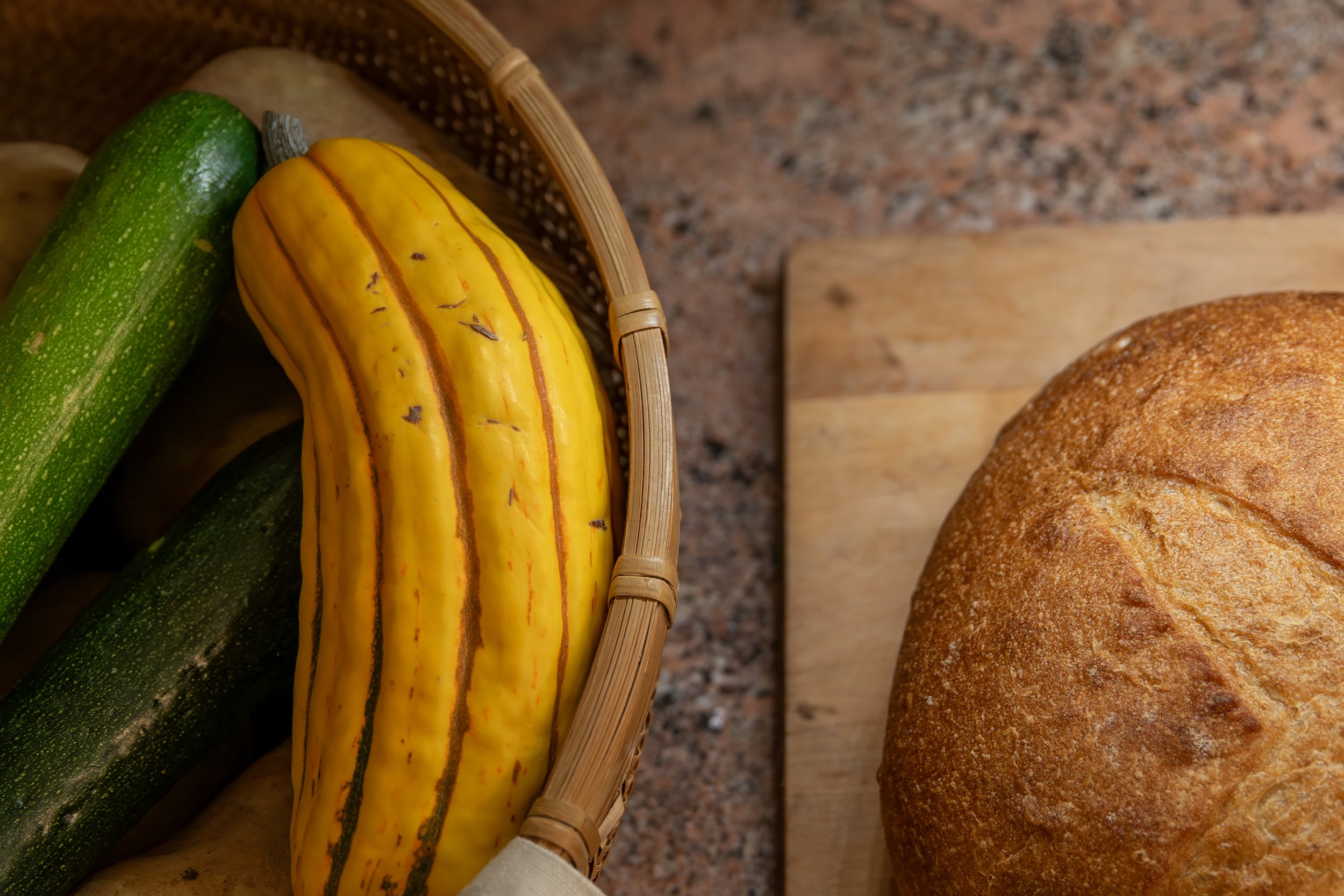 Zucchini and yellow squash in a basket, loaf of bread on a wooden cutting board. Bozeman interior design, interior renovation, and interior styling. 