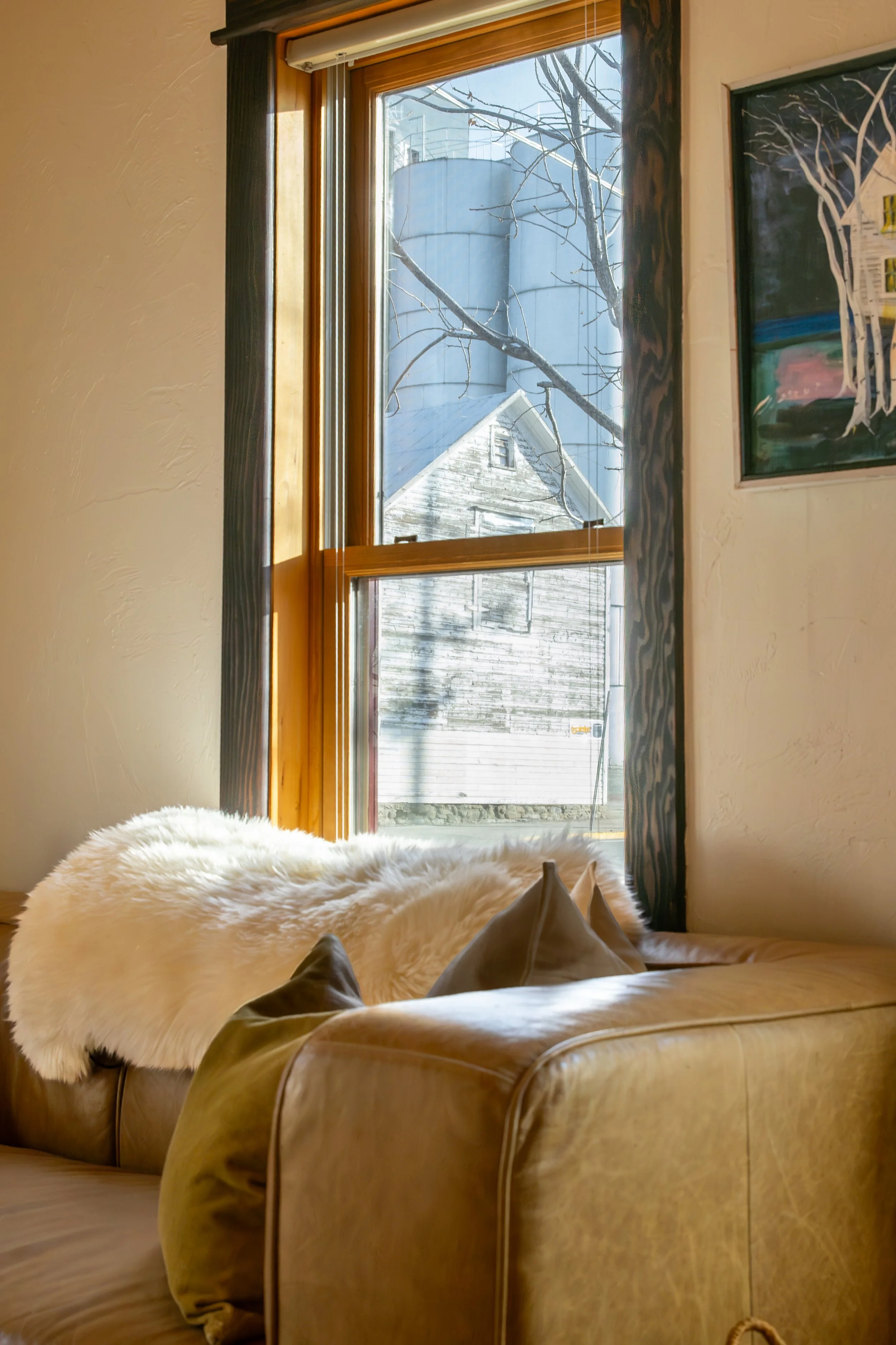 A cozy living room corner with a tan leather sofa, a white furry throw, and beige pillows. Bozeman interior design, interior renovation, and interior styling.