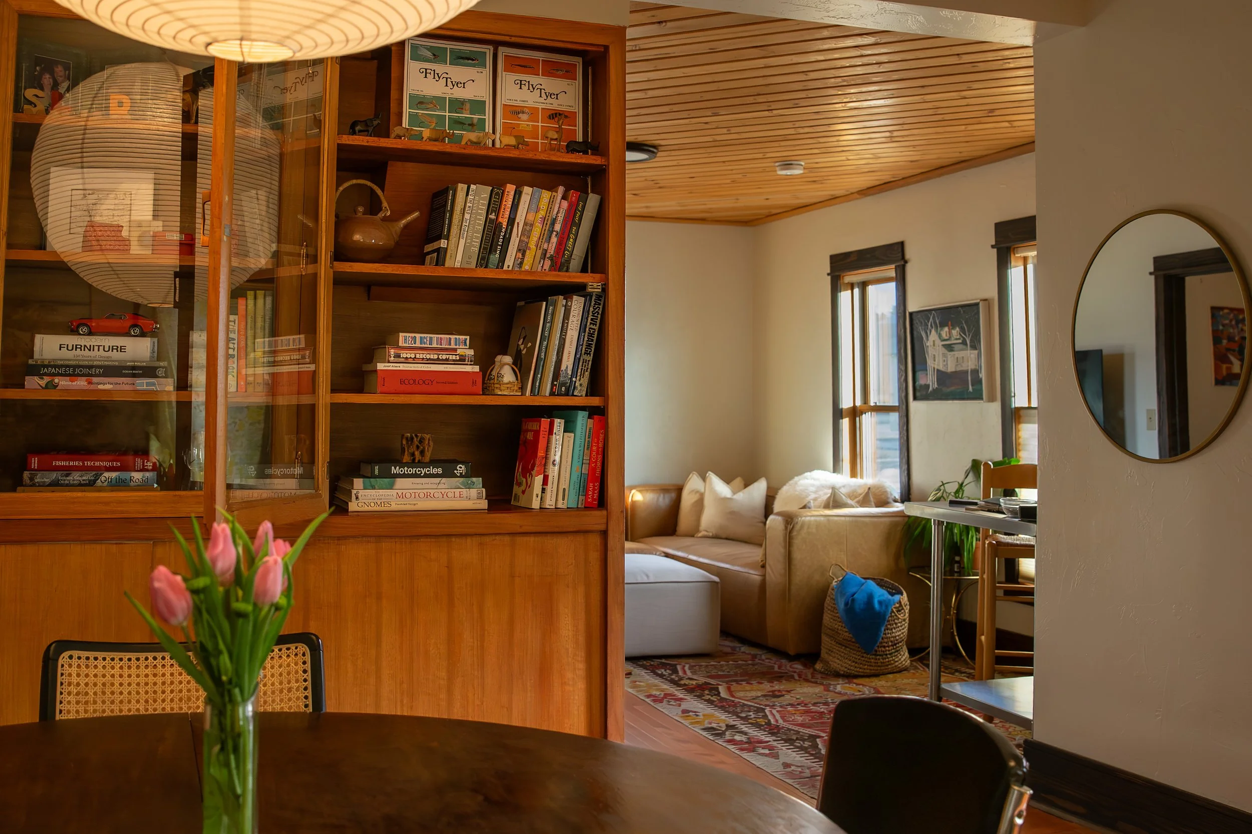A cozy living room with a built-in wooden bookshelf filled with books and decorative items, a beige couch with pillows, and a small table with a plant. Bozeman interior design, interior renovation, and interior styling.