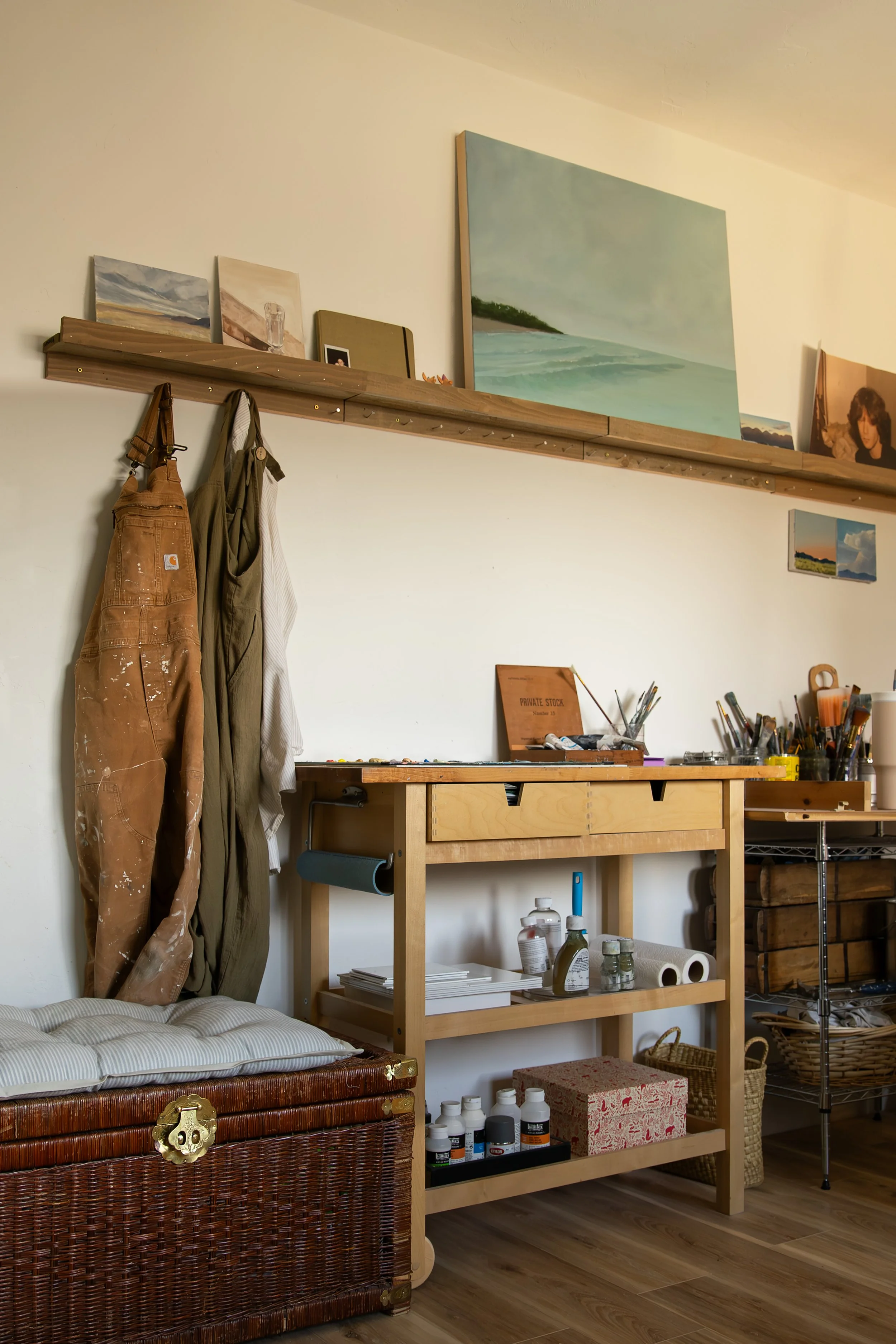 An artist's studio with a wooden worktable, art supplies, and paintings on the wall and bookshelf. Bozeman interior design, interior renovation, and interior styling. 