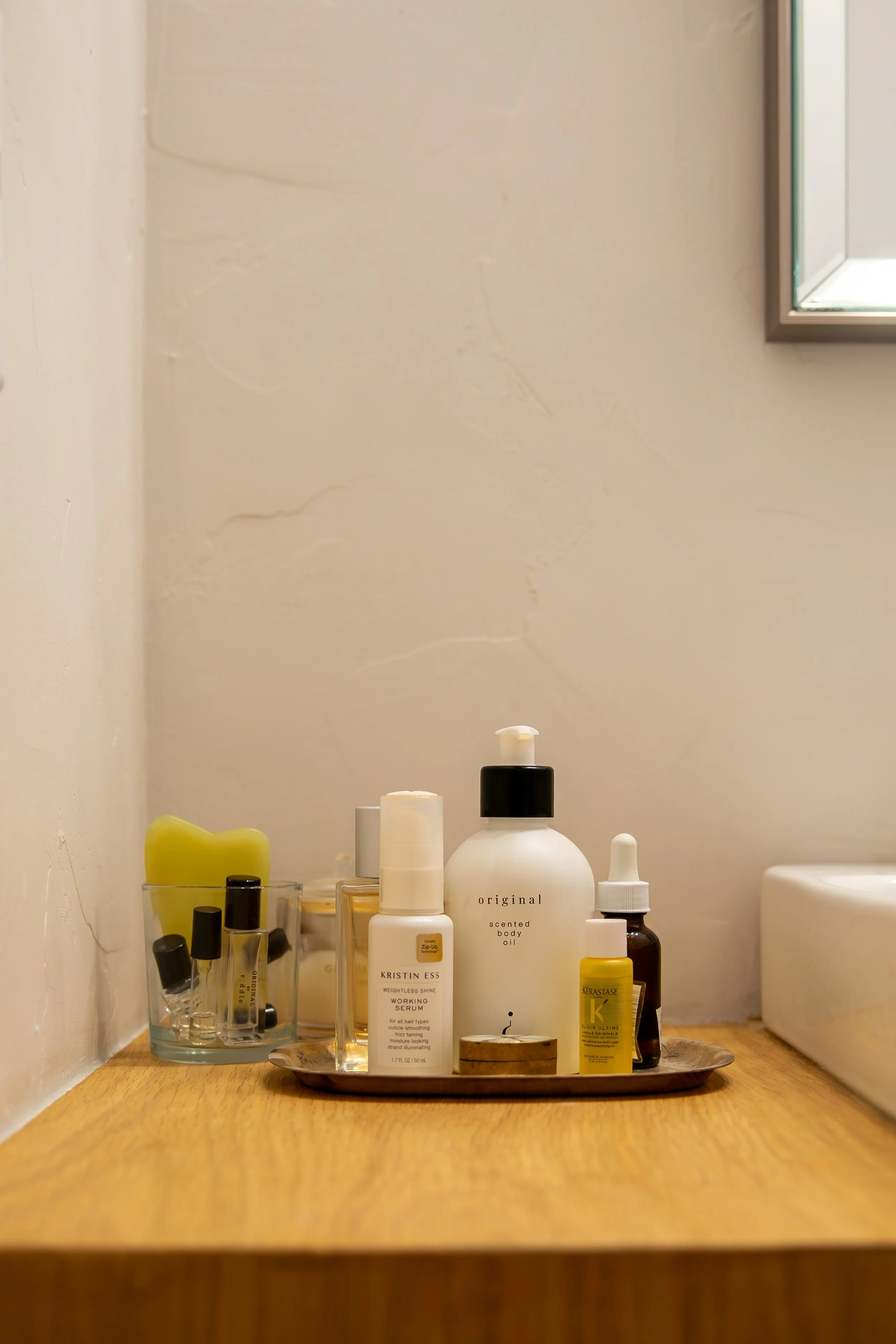 Skincare and cosmetic bottles on a silver tray on a wooden counter, with a beige wall and partial mirror in the background. Bozeman interior design, interior renovation, and interior styling. 