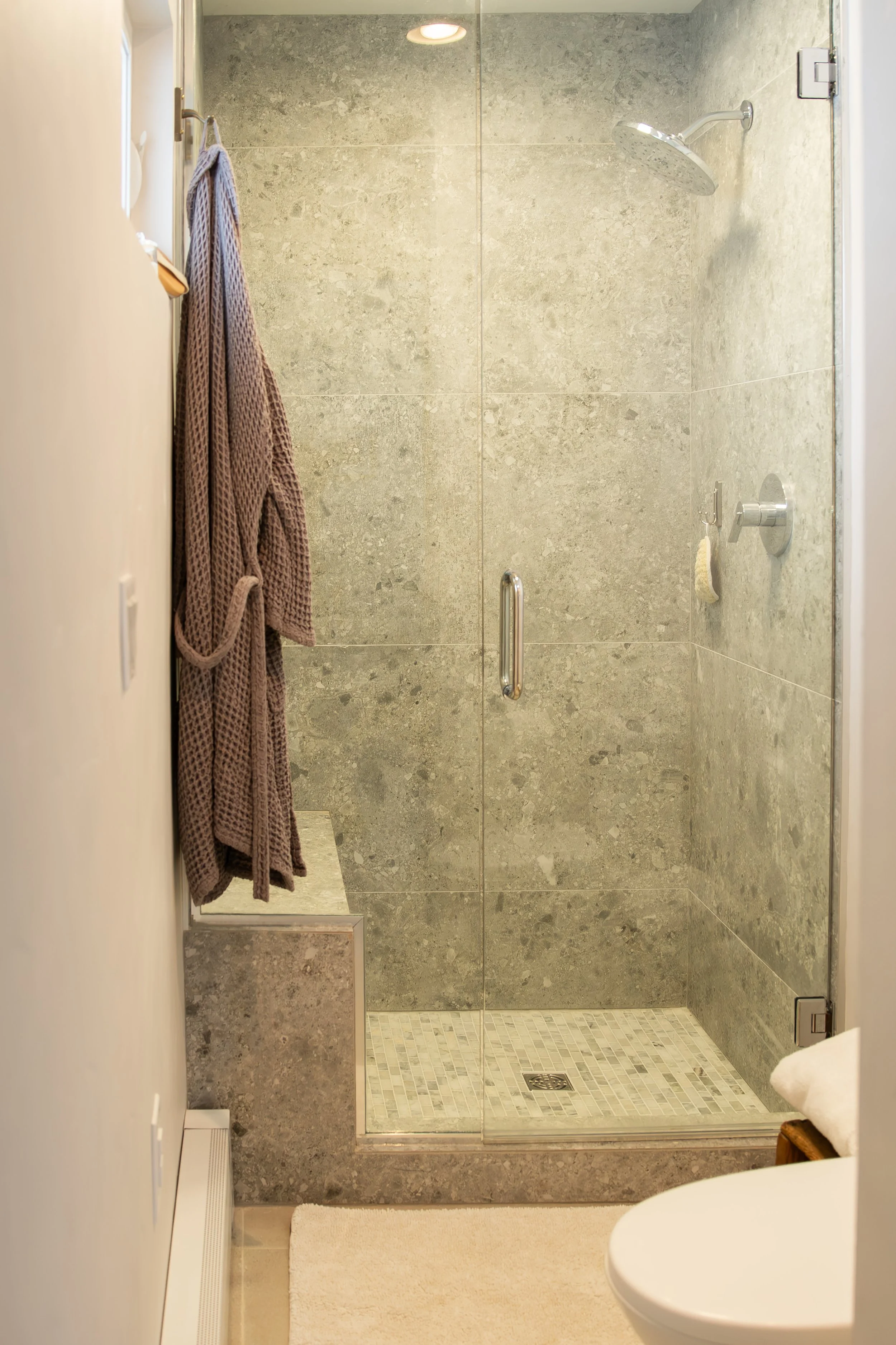 A modern walk-in shower with glass door, grey tiled walls, showerhead, and a small tiled floor area. Bozeman interior design, interior renovation, and interior styling. 