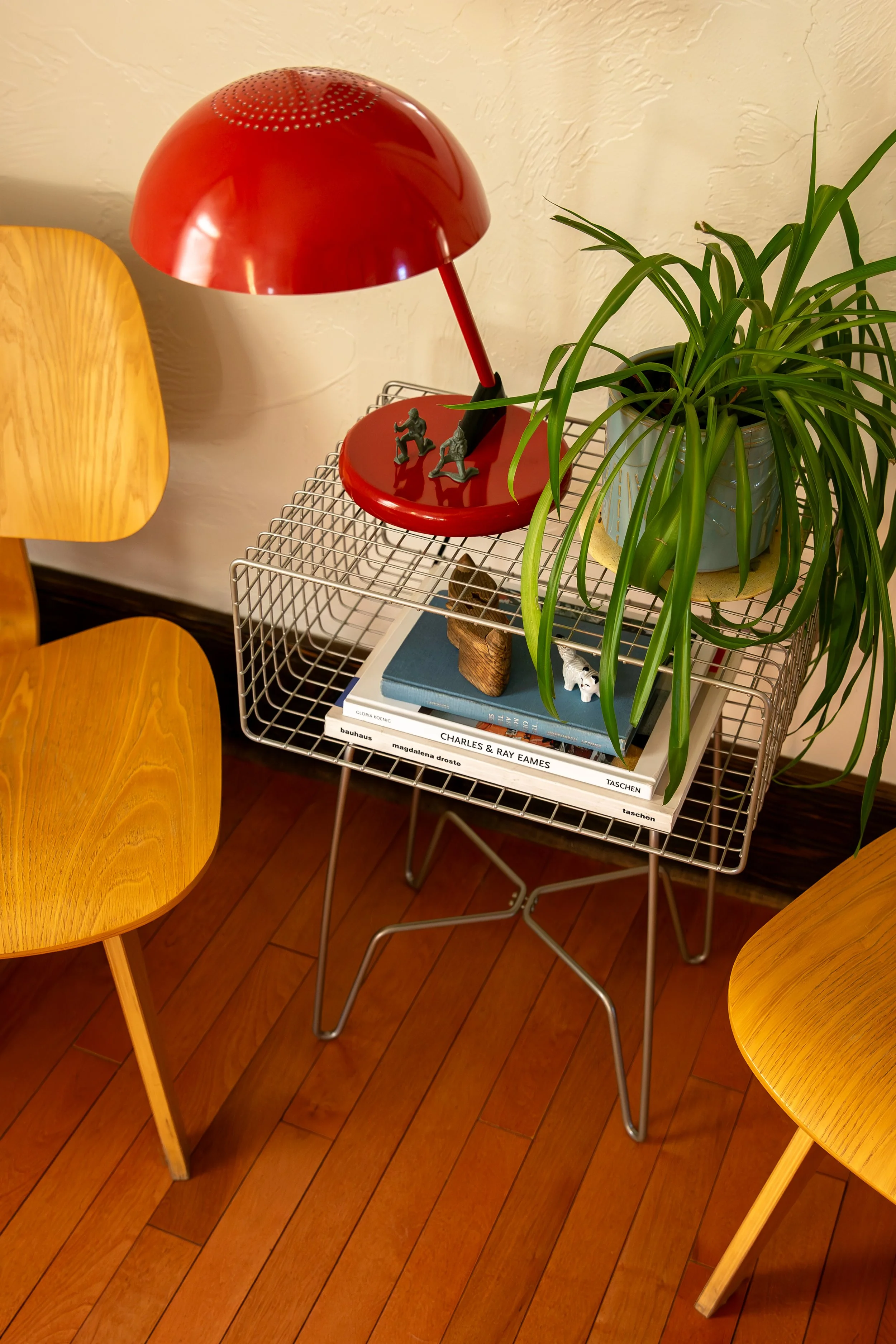 A red desk lamp on a wire side table with potted plant, books, and small decorative items around it, flanked by wooden chairs on a hardwood floor. Bozeman interior design, interior renovation, and interior styling. 