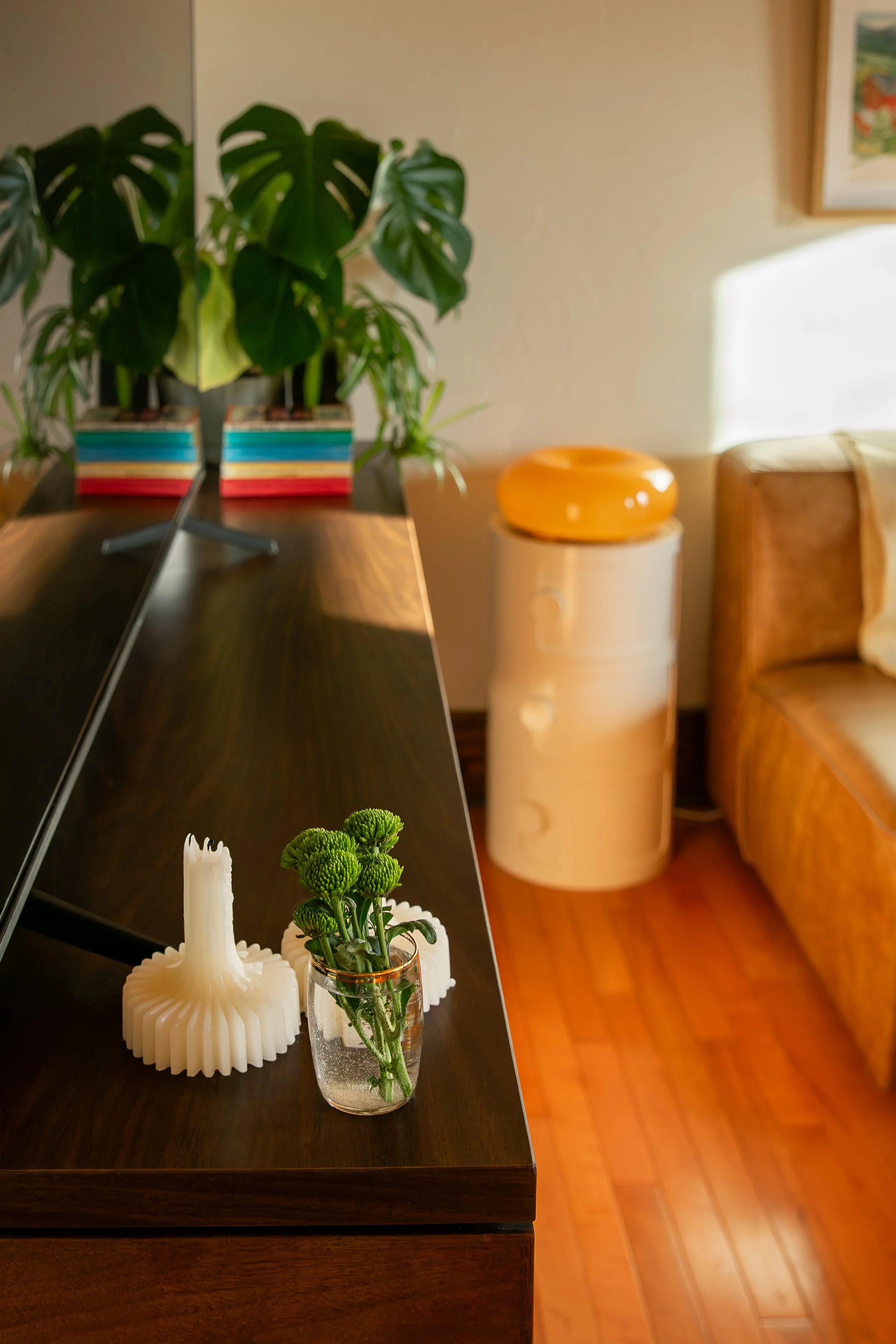 A living room with a wooden table holding a small vase with green chrysanthemums, a white decorative sculpture, and a large houseplant in the background. Bozeman interior design, interior renovation, and interior styling. 