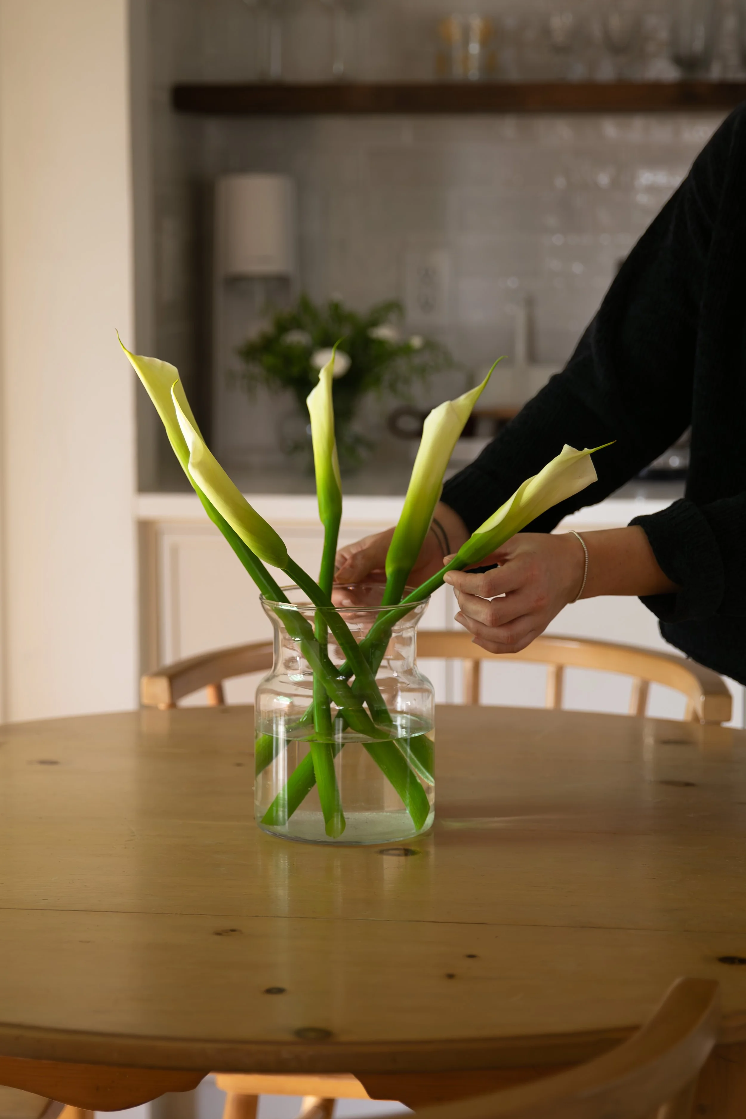Person arranging calla lilies in a glass vase on a wooden table in a home kitchen. Bozeman interior design, interior renovation, and interior styling. 