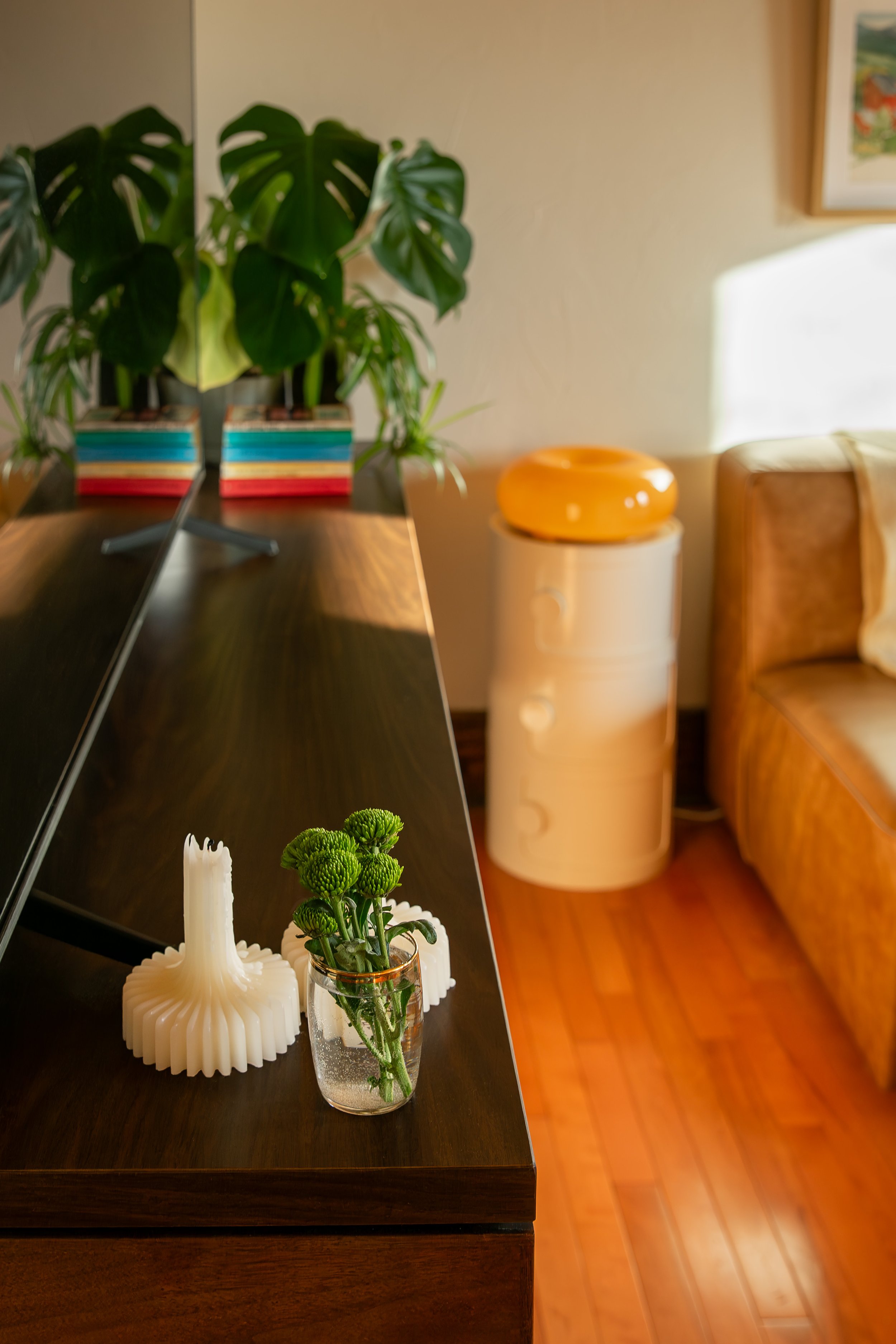 A living room with a wooden sideboard, a potted green plant, and decorative items including a white candle holder, a green plant in a glass container, and a yellow ceramic vessel. Bozeman interior design, interior renovation, and interior styling. 