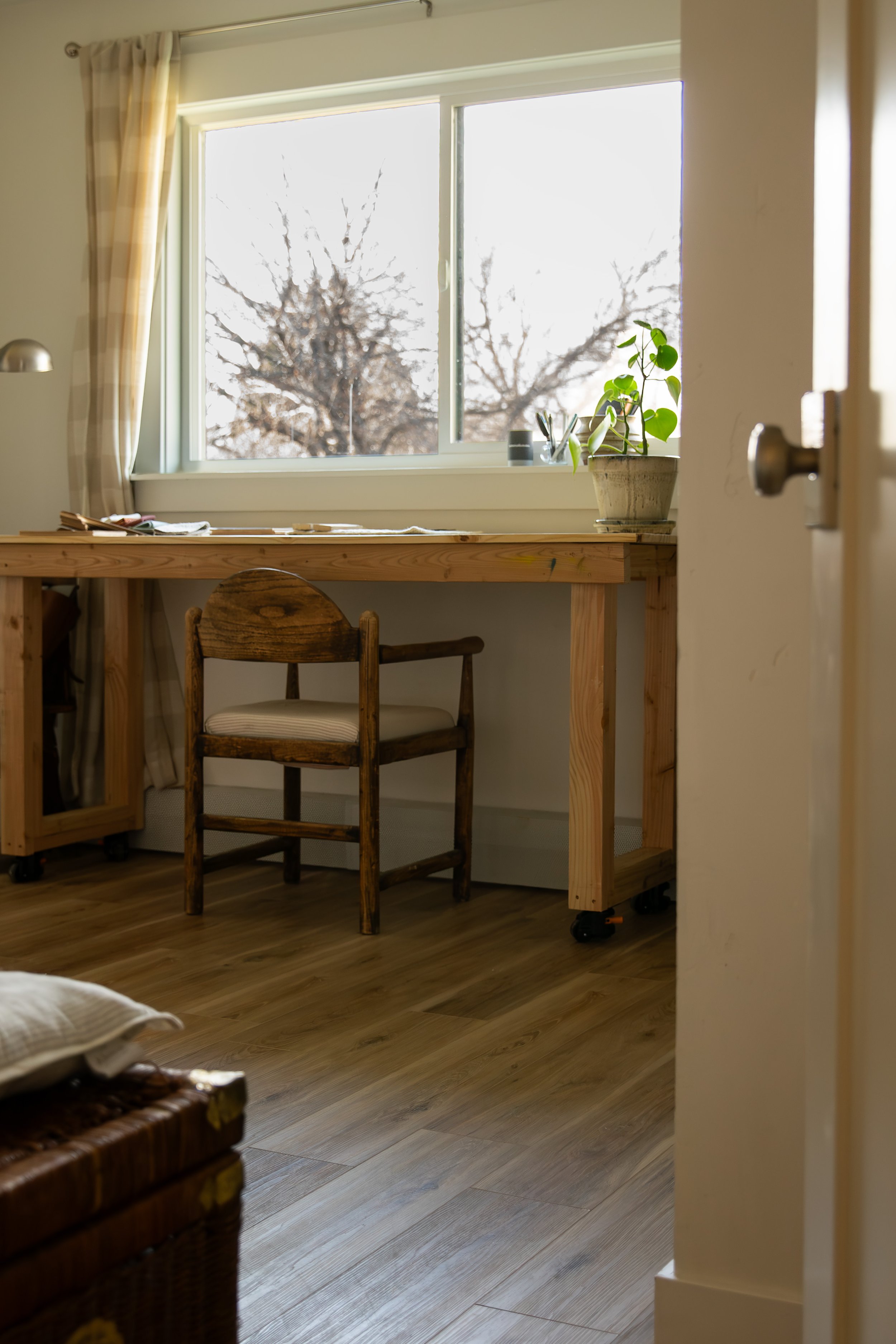 A cozy home office space with a large window, wooden desk, and rustic wooden chair, illuminated by natural light. Bozeman interior design, interior renovation, and interior styling. 