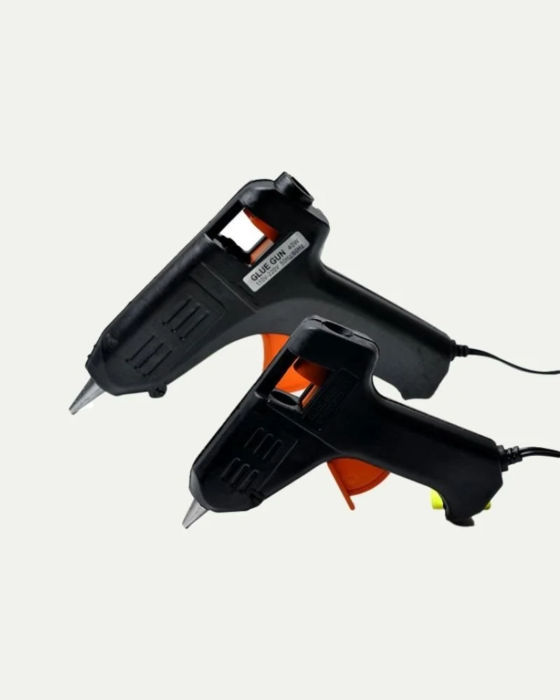 Two black hot glue guns with orange triggers and cords, positioned against a white background.