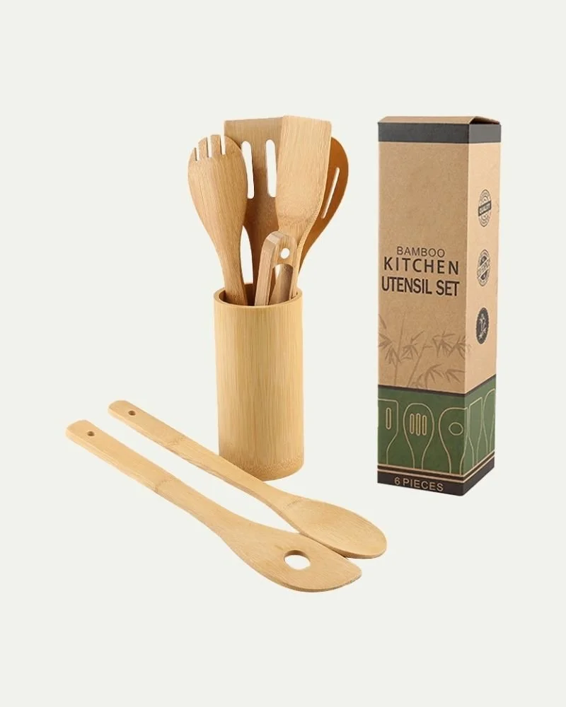 Set of six bamboo kitchen utensils, including spatula, spoon, and tongs, in a cylindrical holder, with two additional utensils lying flat in front, and a box labeled 'Bamboo Kitchen Utensil Set' on a white background.